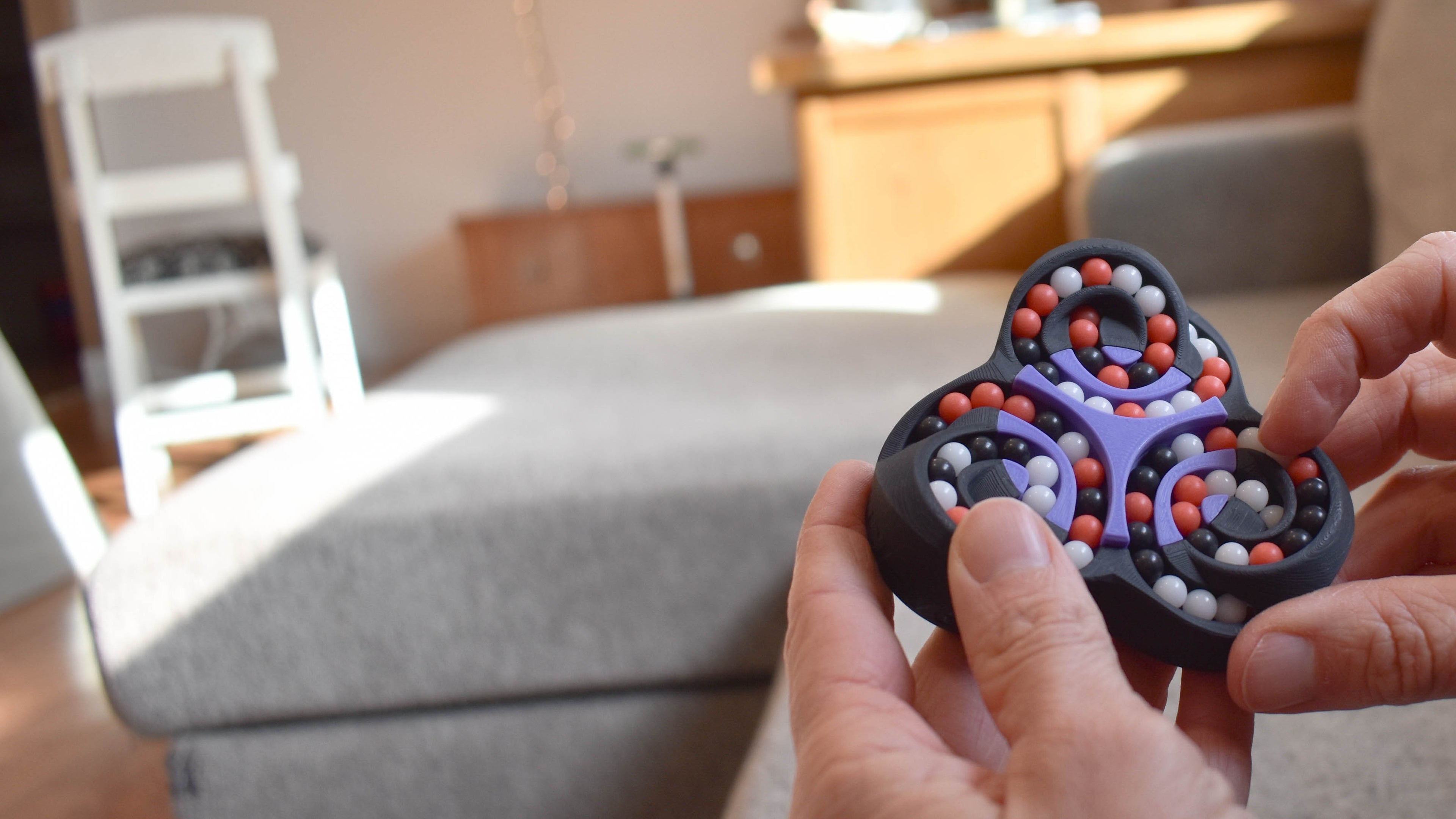 Person holding a black fidget spinner with colorful beads in a living room.