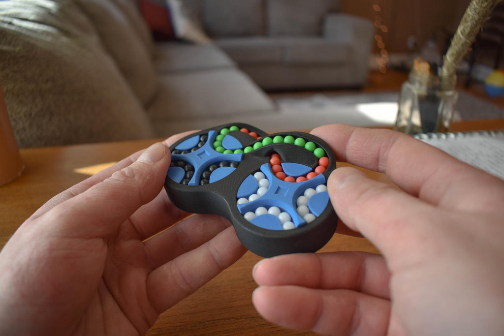 The Figure-Eight mechanical puzzle fidget with four interconnected color-coded sections held in hands. - andEleven - The Figure-Eight (4-Color)