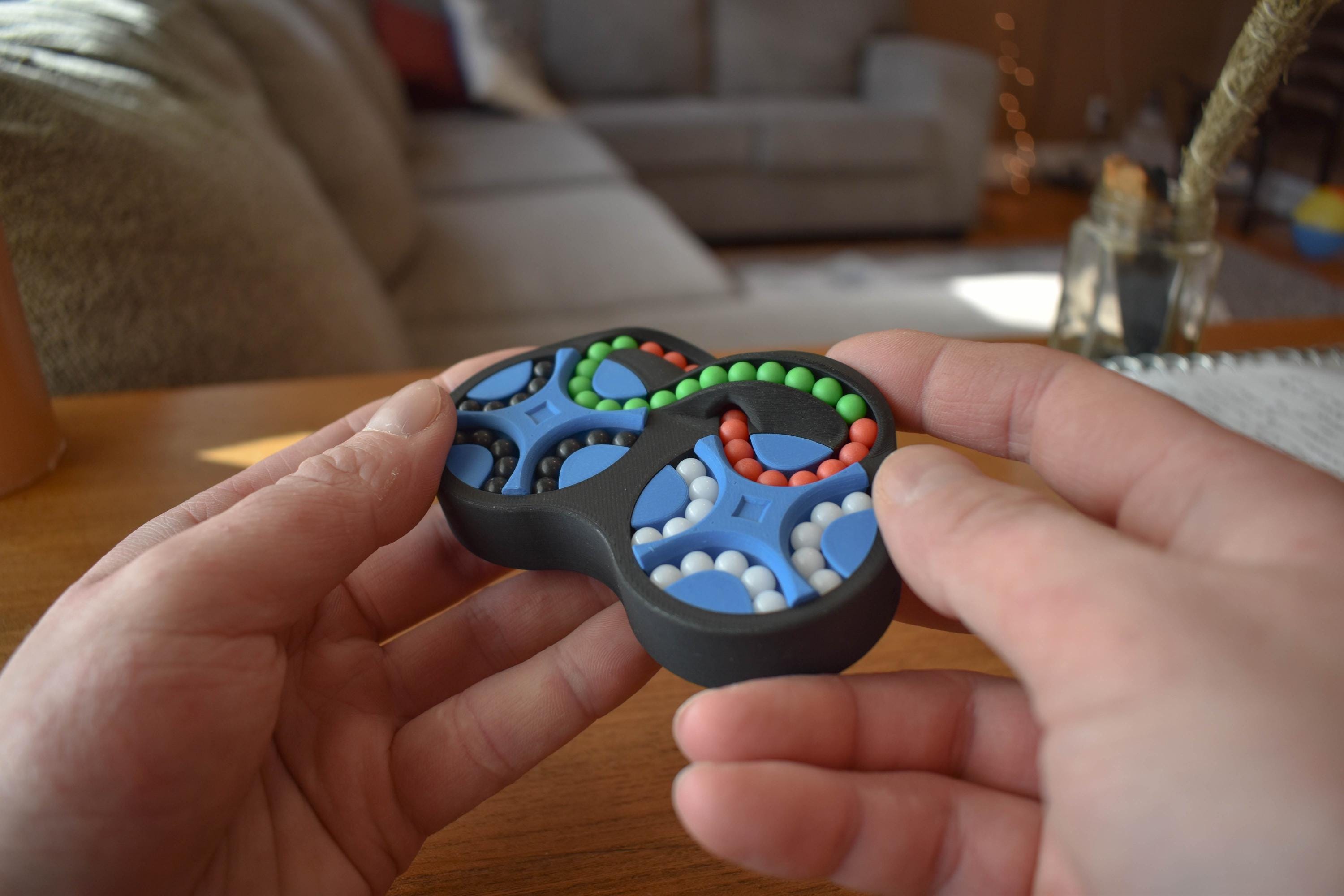 The Figure-Eight mechanical puzzle fidget with four interconnected color-coded sections held in hands. - andEleven - The Figure-Eight (4-Color)