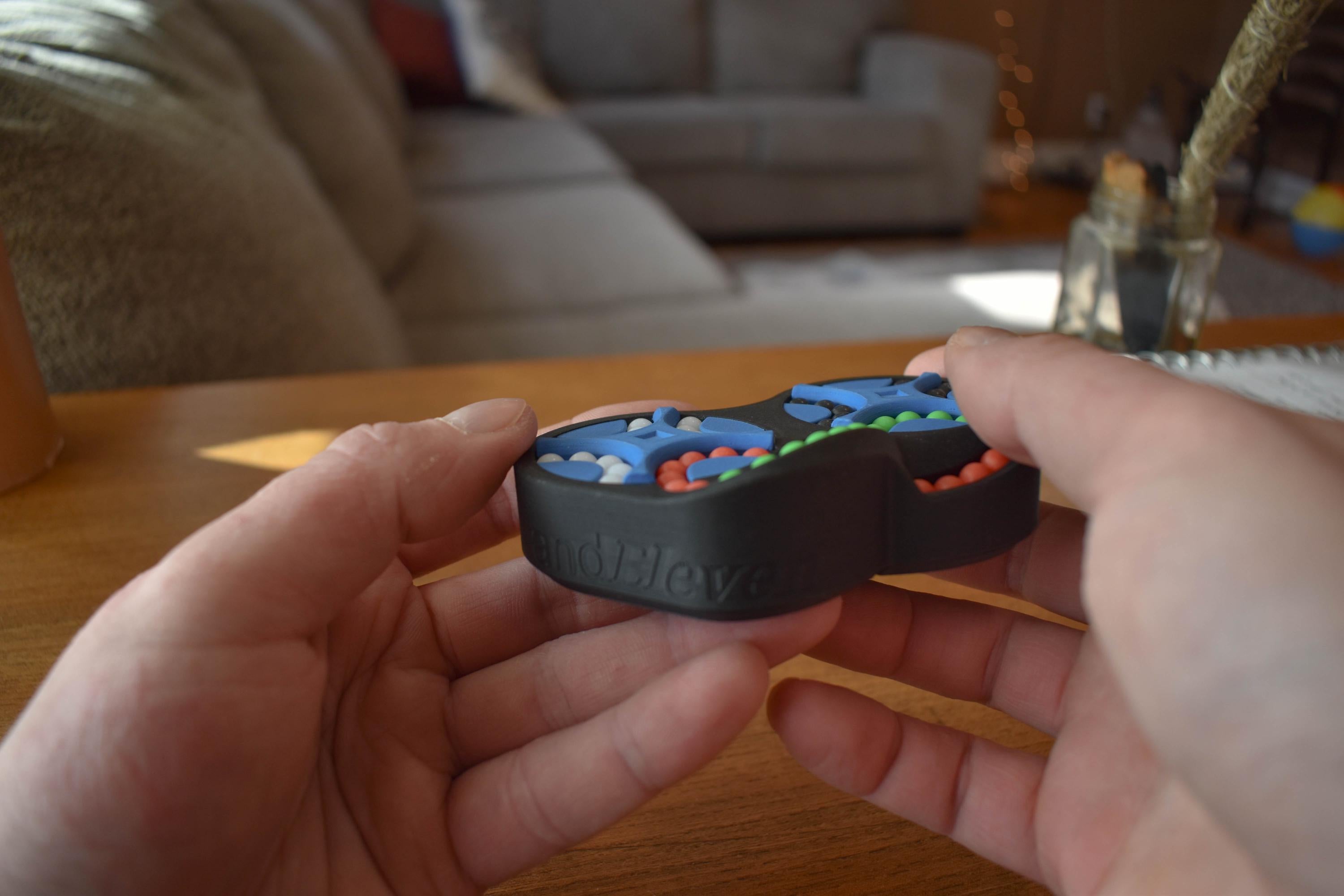 Four-color mechanical puzzle brainteaser held in hands, featuring interlocking circular design and colorful beads for fidget . - andEleven - The Figure-Eight (4-Color)