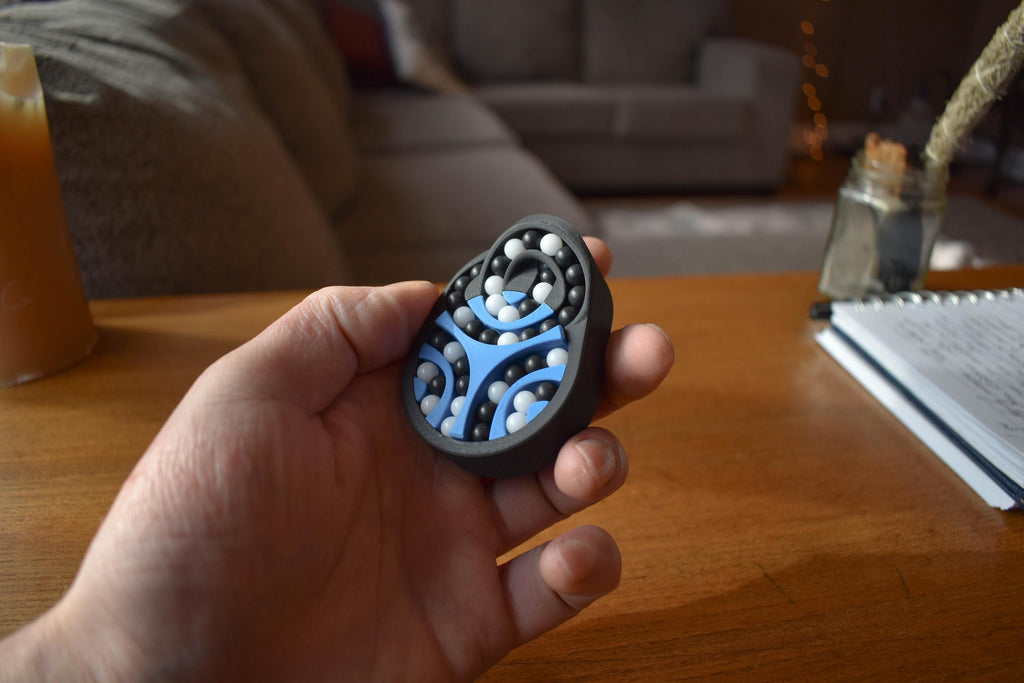 Hand holding blue and black mechanical puzzle brainteaser fidget with metal ball bearings on wooden table background. - andEleven - The Pretzel