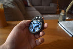 Hand holding blue and black mechanical puzzle brainteaser fidget with metal ball bearings on wooden table background. - andEleven - The Pretzel