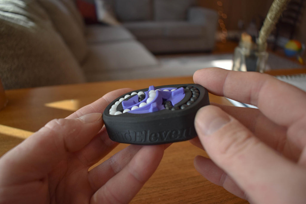 Compact black and purple mechanical puzzle brainteaser fidget held between hands on wooden table. - andEleven - The Infinity (2-Color)