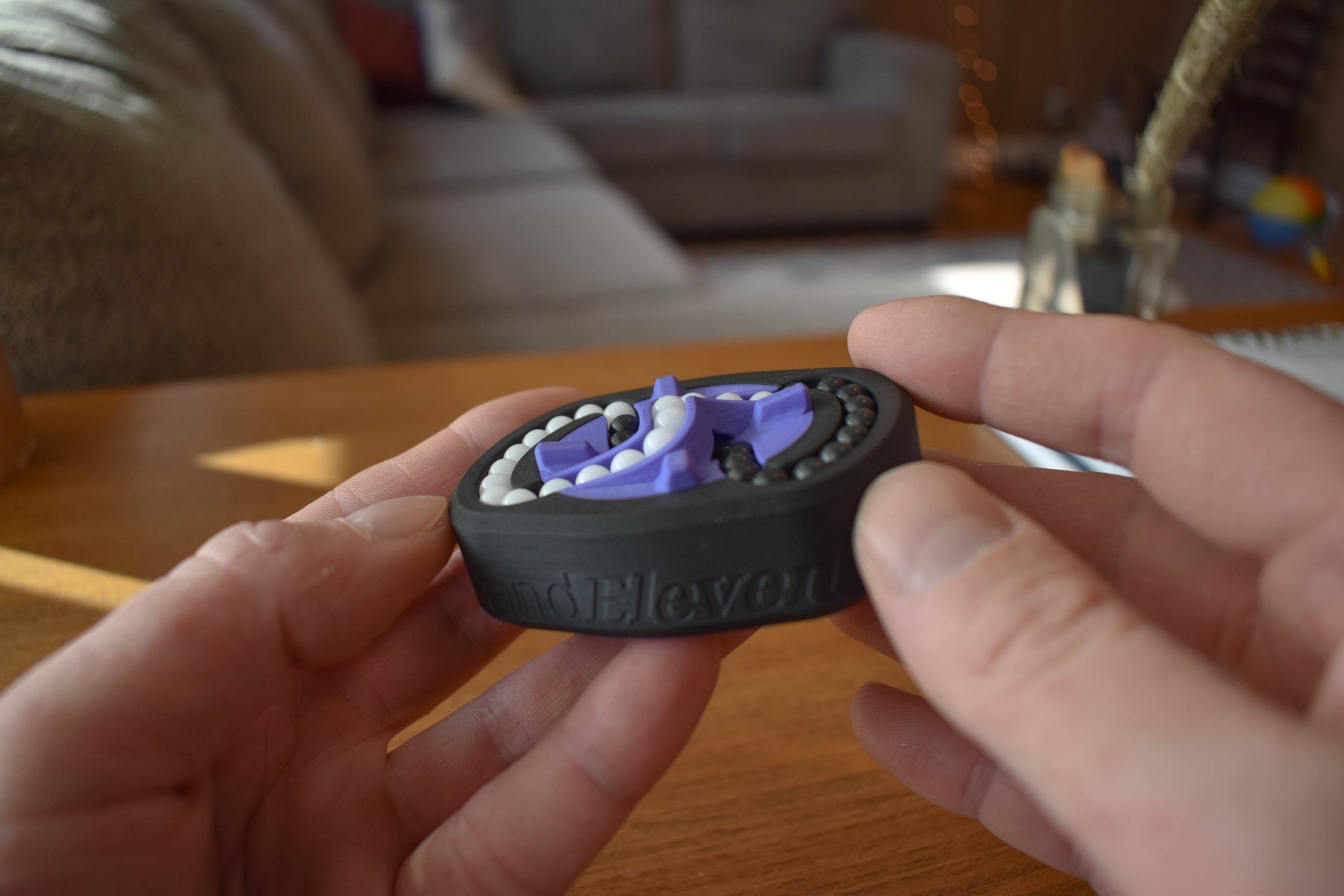 Compact black and purple mechanical puzzle brainteaser fidget held between hands on wooden table. - andEleven - The Infinity (2-Color)