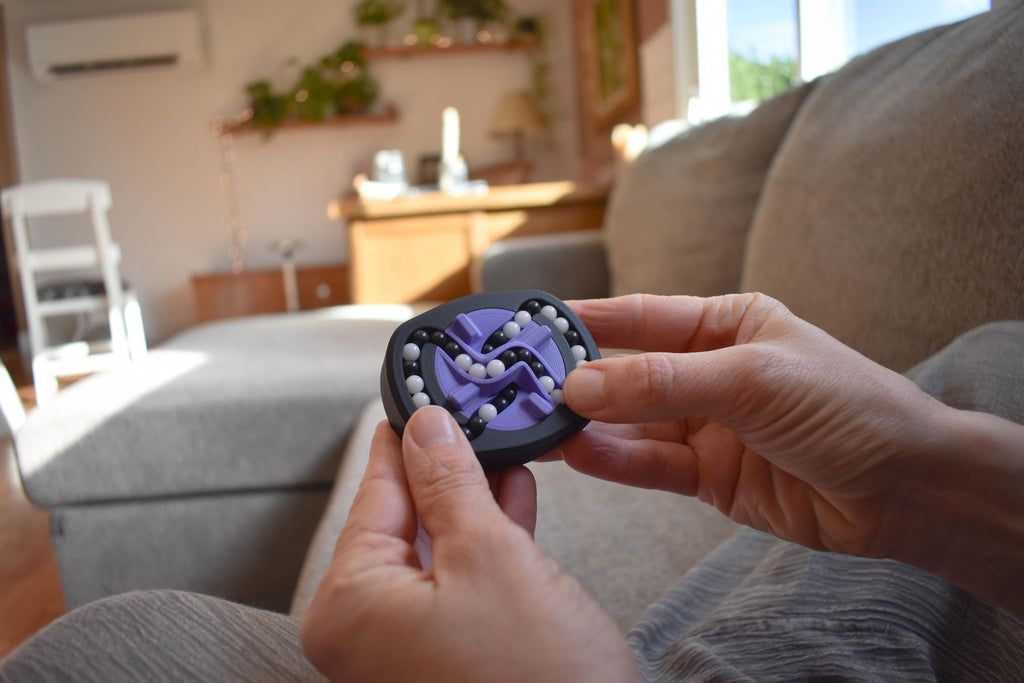 Black and purple mechanical puzzle brainteaser fidget held in hands on couch background. - andEleven - The Infinity (2-Color)