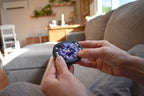 Hands holding a purple and black mechanical puzzle brainteaser fidget on a couch background. - andEleven - The Infinity (2-Color)
