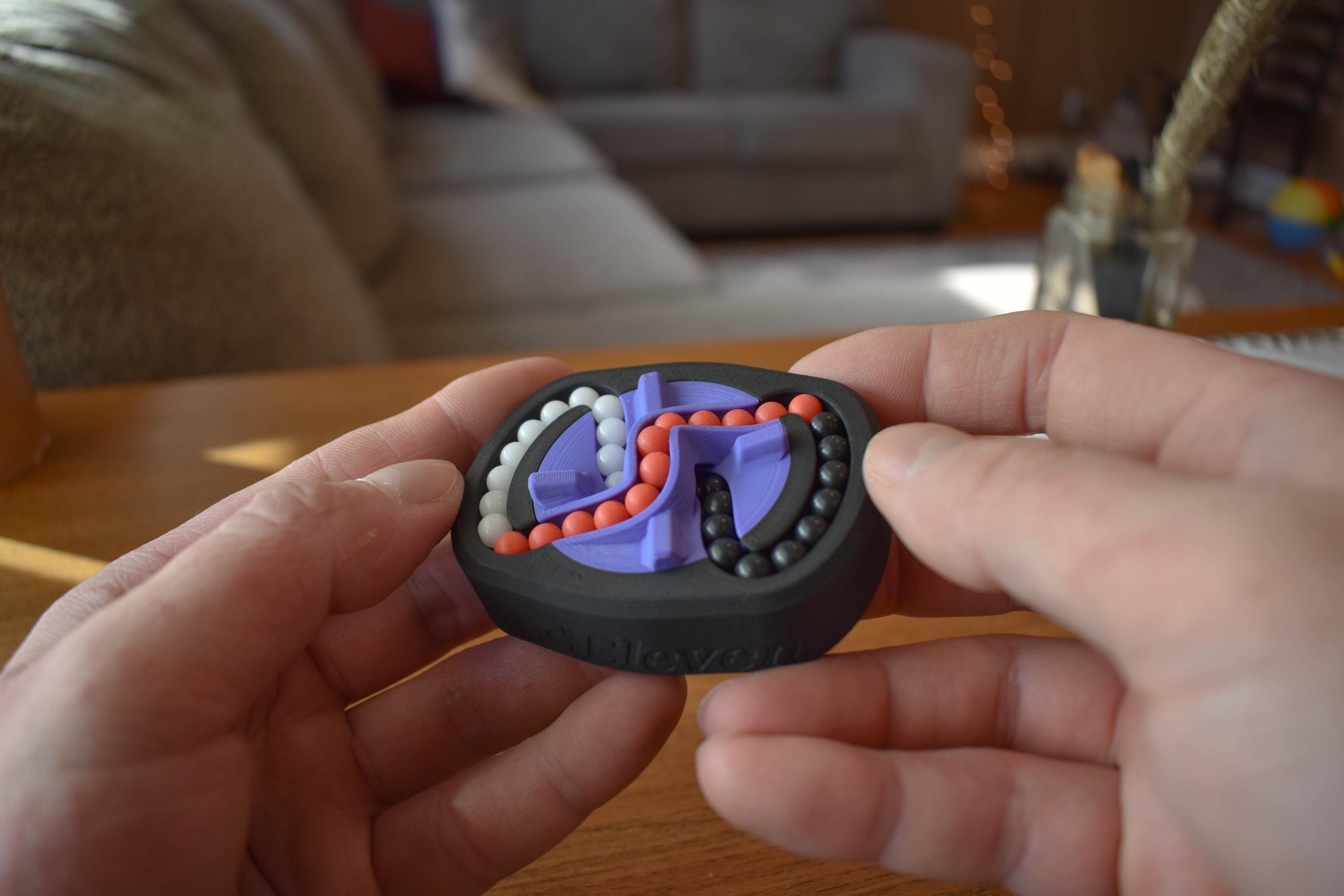 Compact three-color mechanical puzzle fidget with interlocking purple, red, and blue pieces held in hands on wooden table. - andEleven - The Infinity (3-Color)