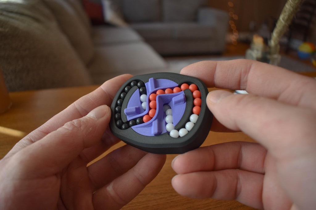 Compact black mechanical puzzle with interlocking tracks and red, white, and purple beads for brainteaser fidget play. - andEleven - The Infinity (3-Color)