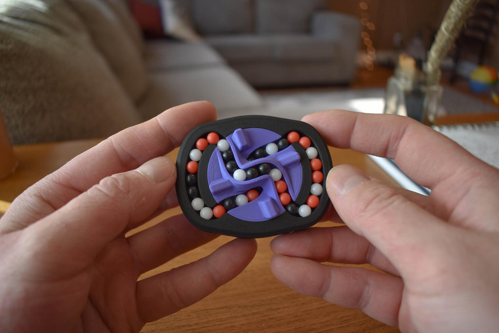 Compact black mechanical puzzle with purple rotating pieces and red, white beads, held in hands as brainteaser fidget toy. - andEleven - The Infinity (3-Color)