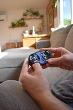 Hands holding a small black and blue mechanical puzzle brainteaser fidget on a gray couch. - andEleven - The Butterfly