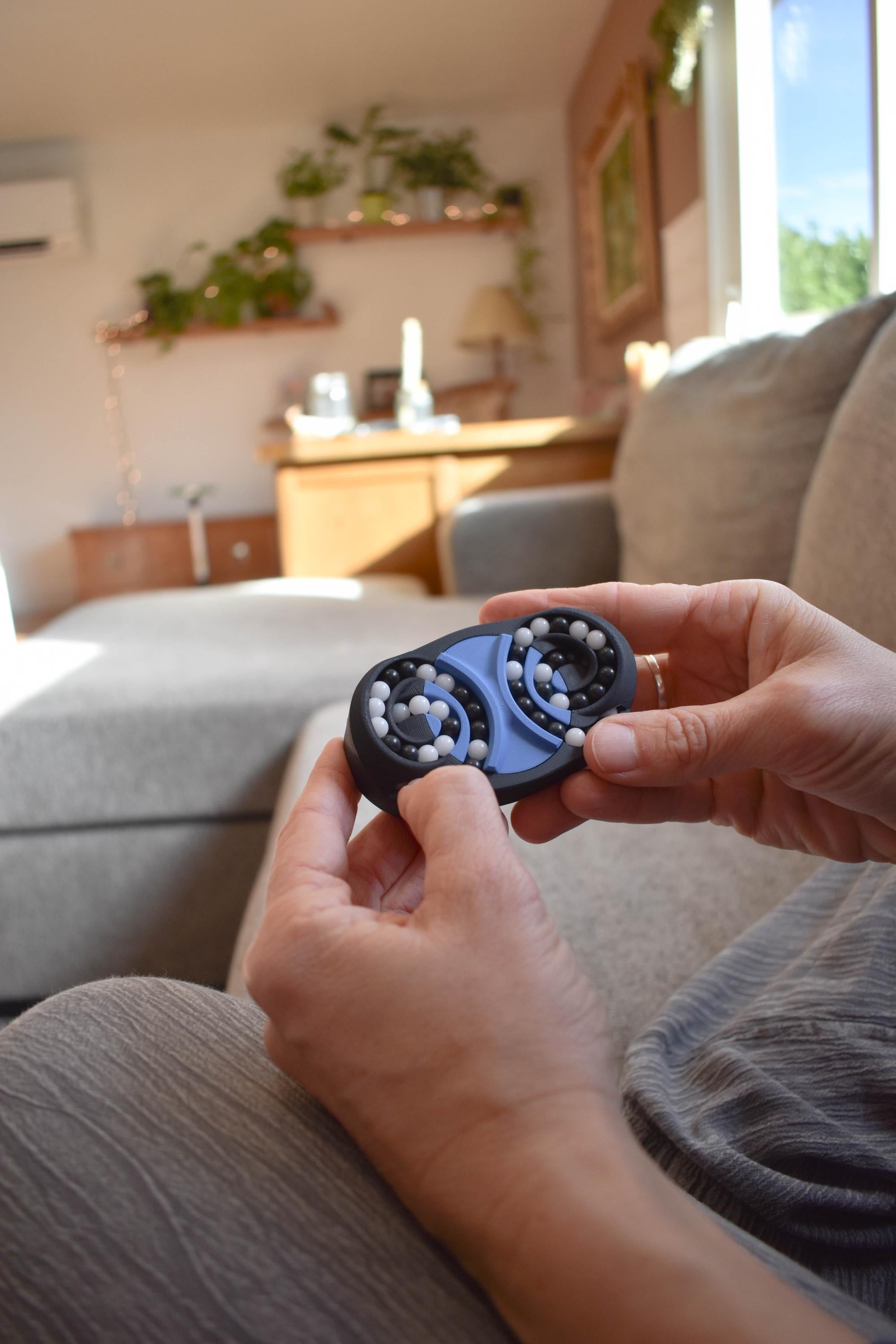 Hands holding a small black and blue mechanical puzzle brainteaser fidget on a gray couch. - andEleven - The Butterfly