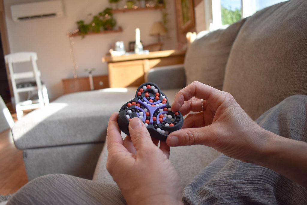 Hands holding a black and red mechanical puzzle brainteaser fidget in a cozy living room setting. - andEleven - The Triad