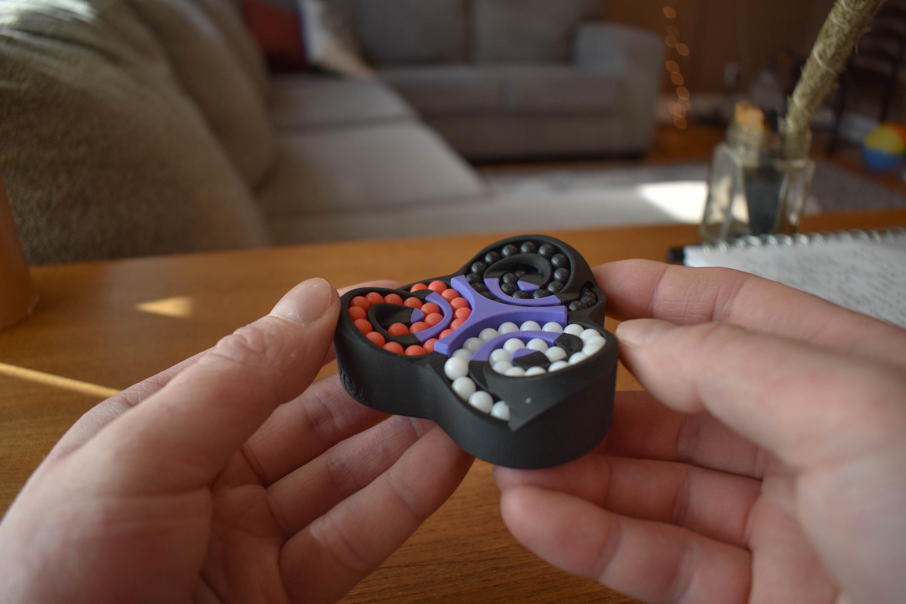 Black triangular mechanical puzzle with three circular colorful bead tracks held in hands, brainteaser fidget toy. - andEleven - The Triad