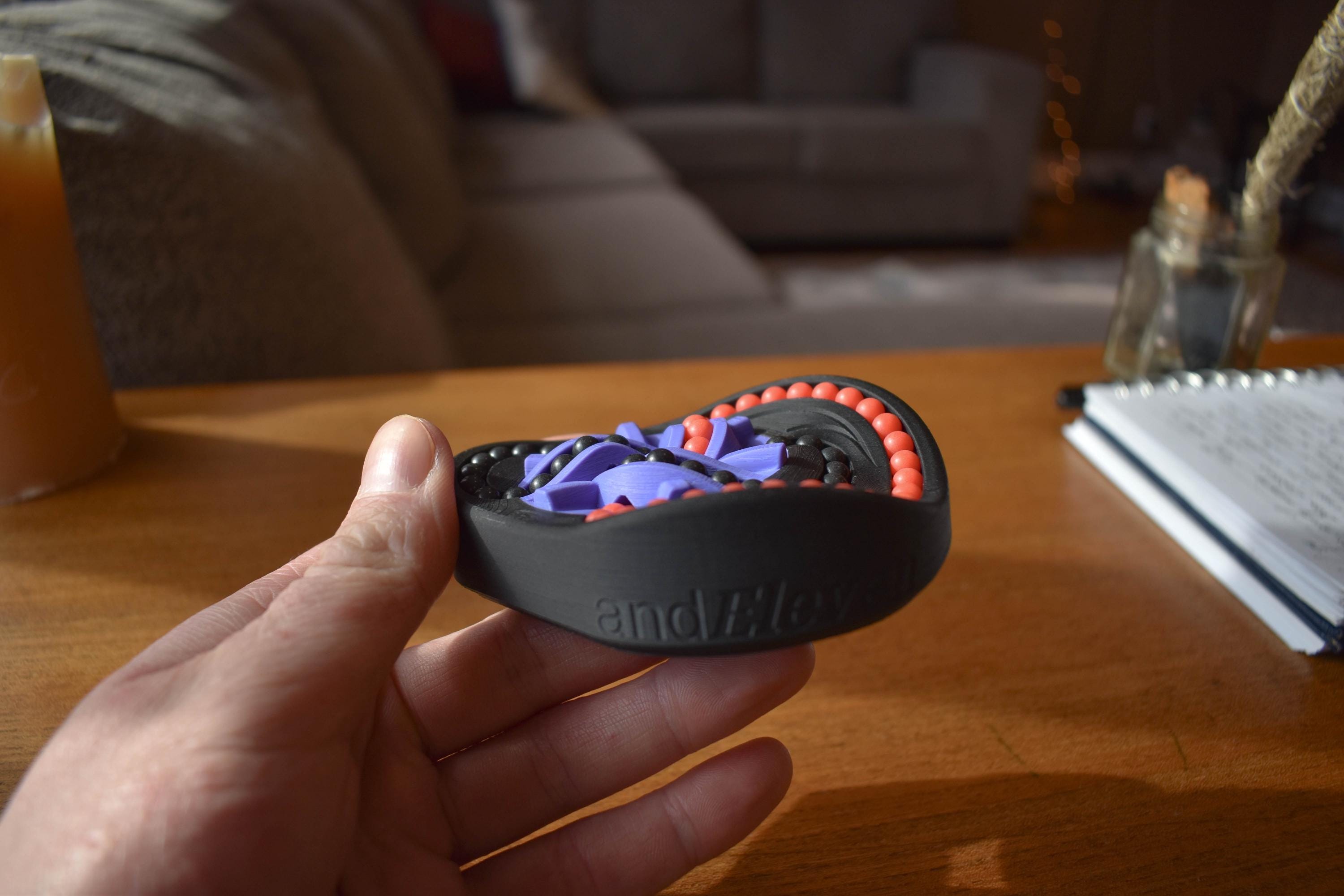 Compact round mechanical puzzle in black and purple, designed as a fidget brainteaser held in hand. - andEleven - The Taurus (2-Color)