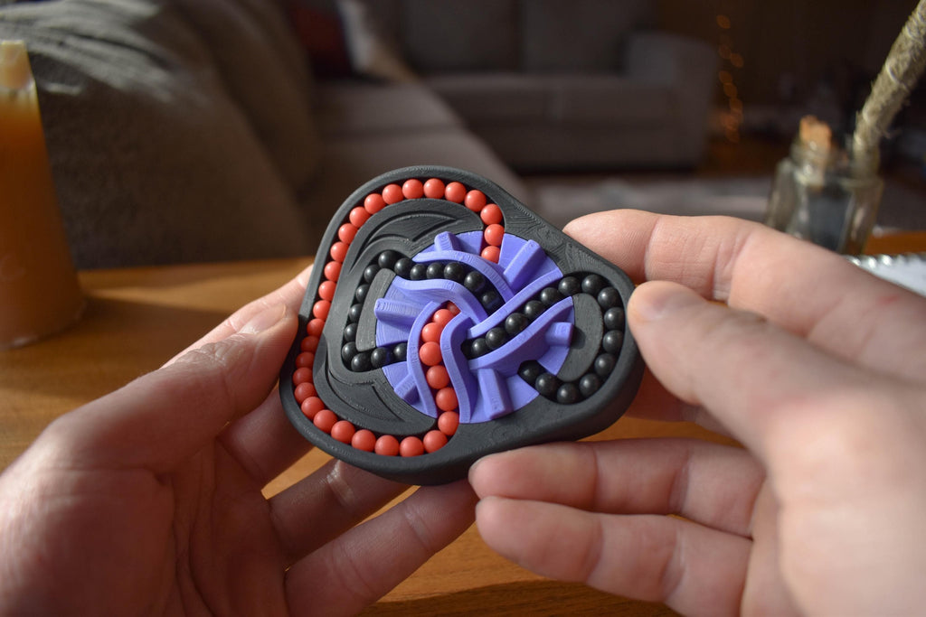 Two-color mechanical puzzle brainteaser with interlocking red and purple loops in hands. - andEleven - The Taurus (2-Color)