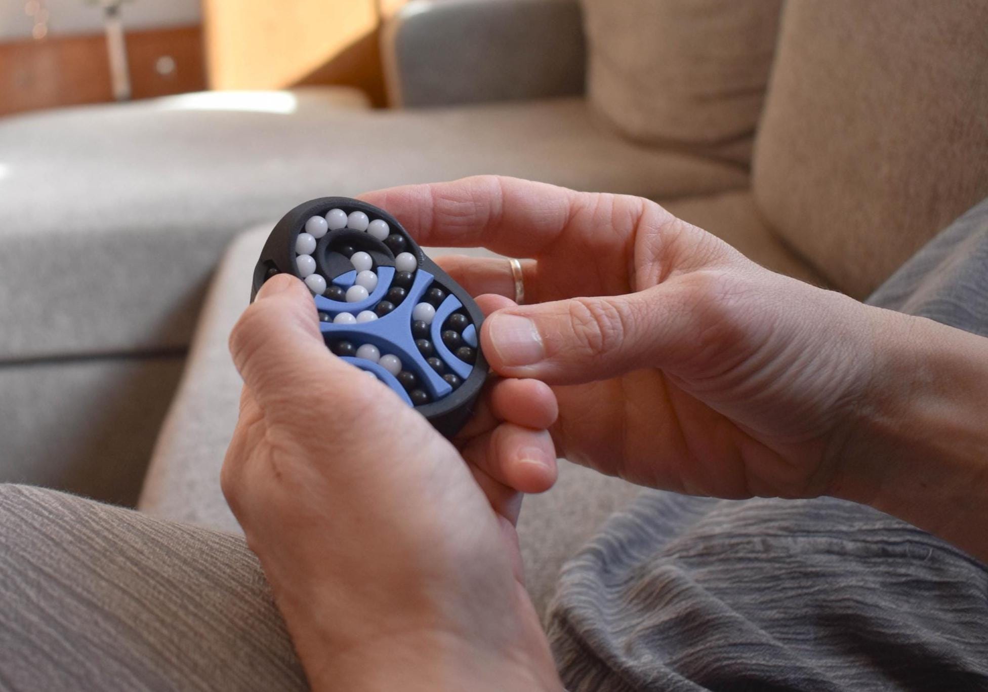 Compact black and blue mechanical puzzle held in hands, designed as a brainteaser and fidget toy. - andEleven - The Pretzel