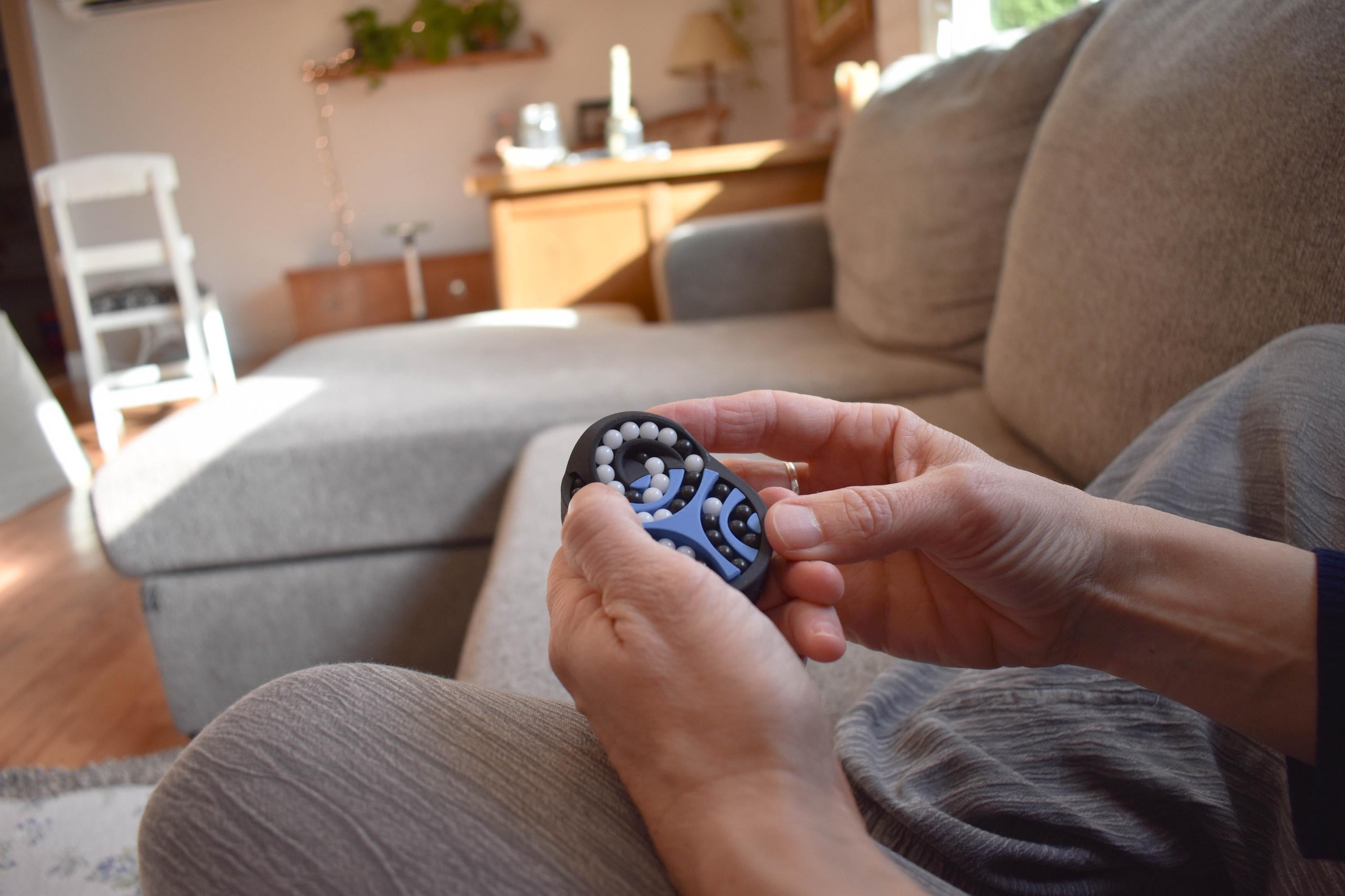 Hands holding a blue and black Pretzel mechanical puzzle brainteaser fidget on a cozy couch. - andEleven - The Pretzel