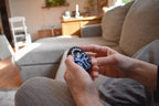 Hands holding a black and silver mechanical puzzle brainteaser fidget with interconnected rings on a gray sofa. - andEleven - The Pretzel