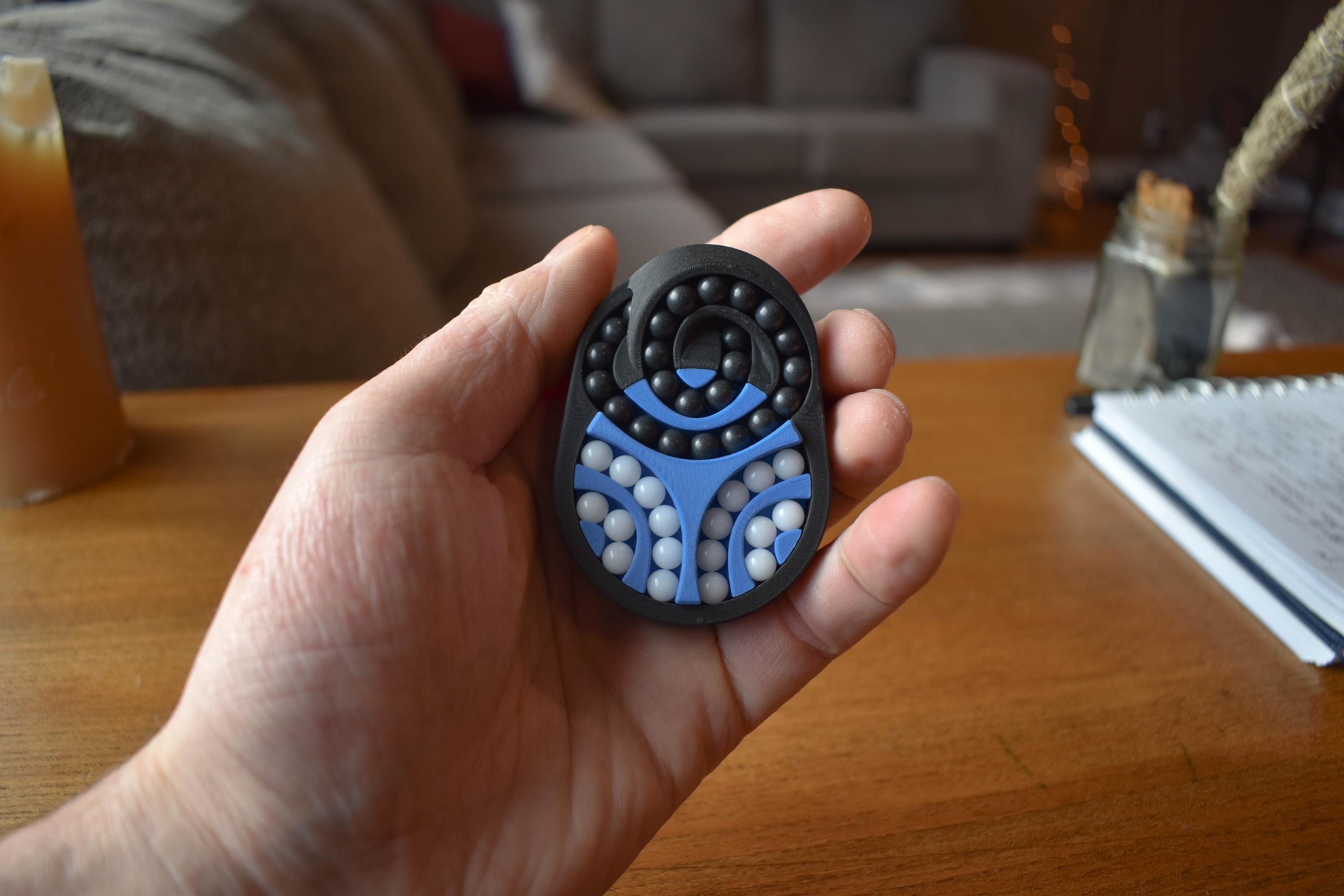 Black and blue mechanical puzzle brainteaser fidget with circular and curved shapes held in hand. - andEleven - The Pretzel