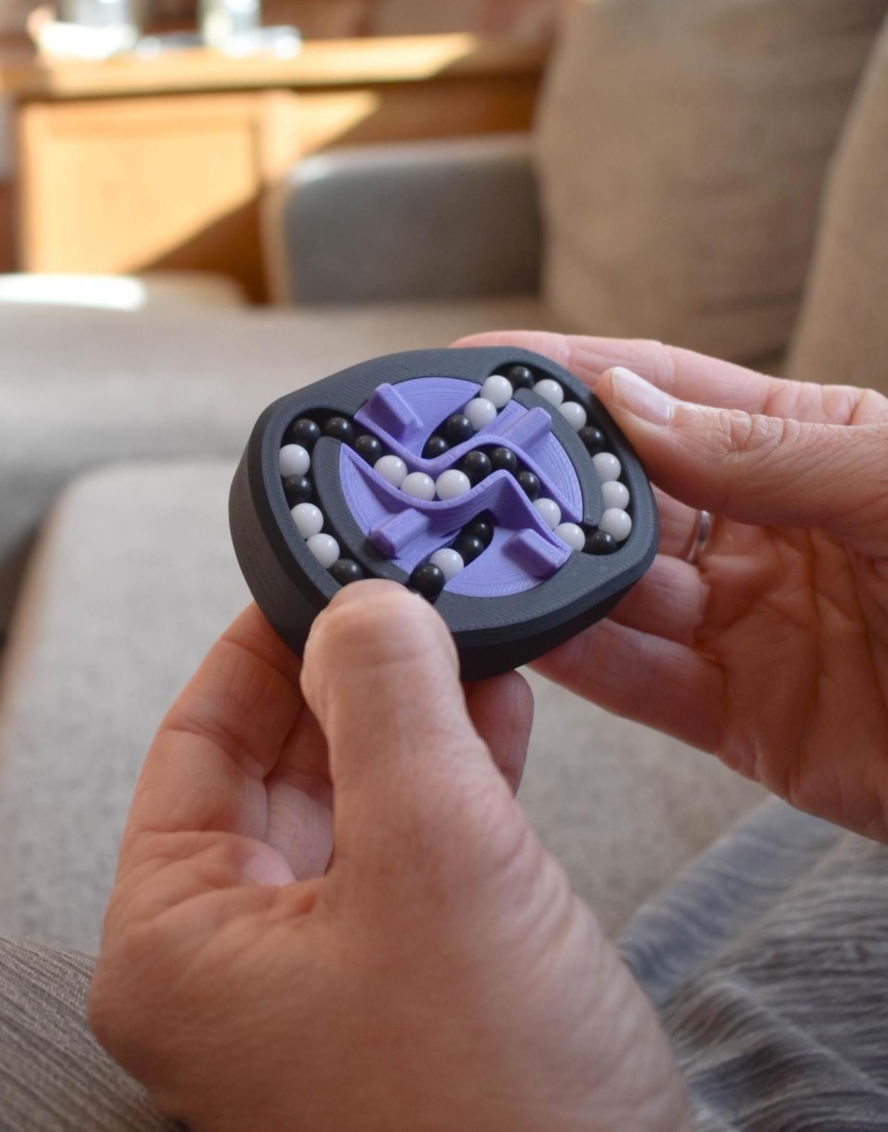 Compact black and purple mechanical puzzle brainteaser with silver ball bearings held in hands, designed as a fidget toy. - andEleven - The Infinity (2-Color)