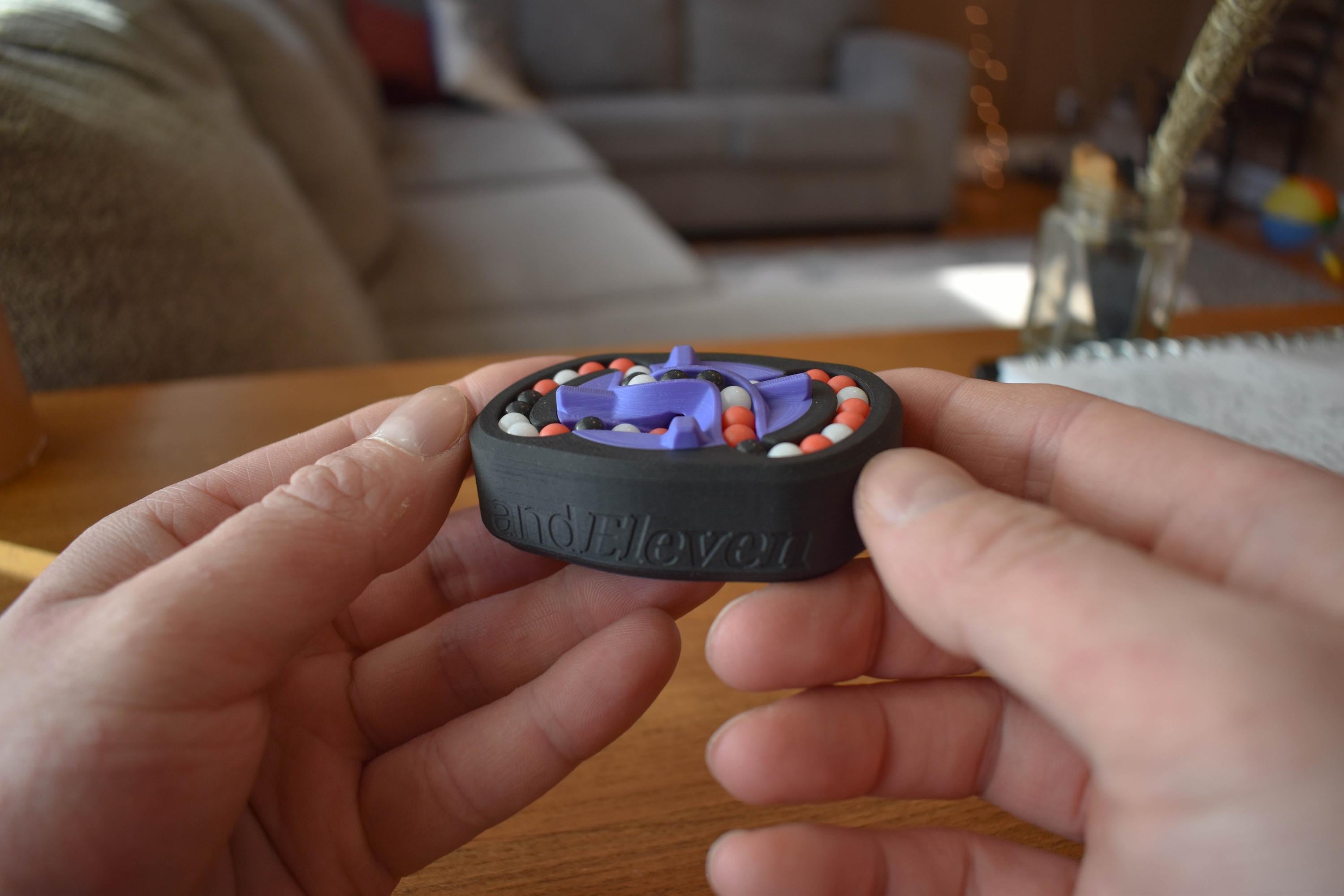 Compact black mechanical puzzle with blue and orange pieces held for fidget and brainteaser use. - andEleven - The Infinity (3-Color)