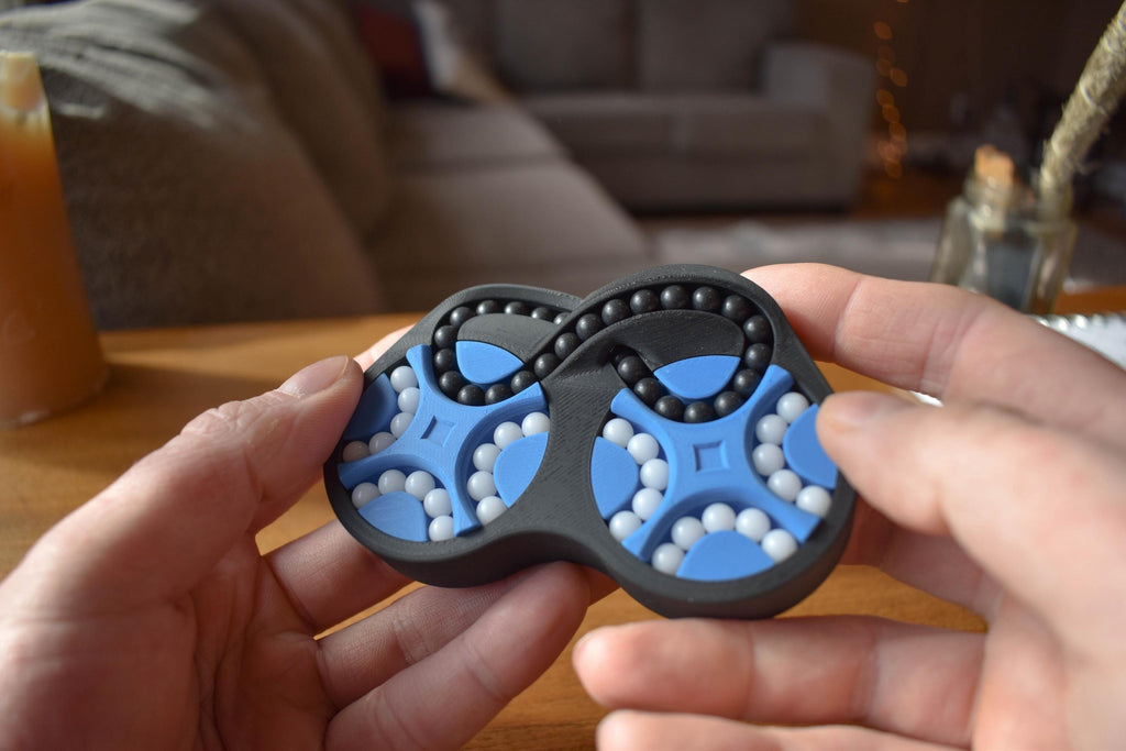 Blue and black figure-eight mechanical puzzle brainteaser fidget with white beads in hands. - andEleven - The Figure-Eight (2-Color)