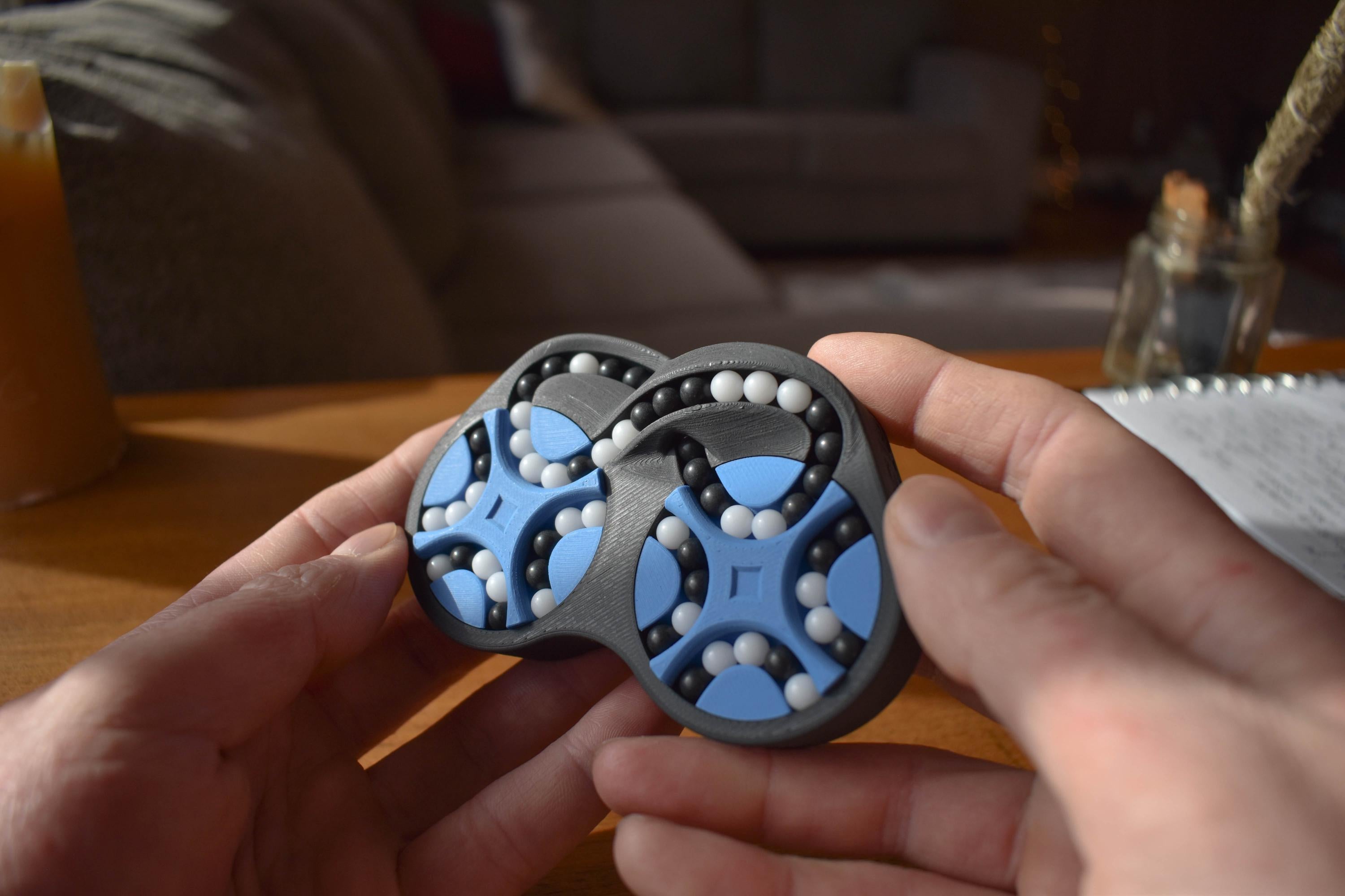 Two-color mechanical puzzle with interlocking blue and black pieces held as a brainteaser fidget toy. - andEleven - The Figure-Eight (2-Color)