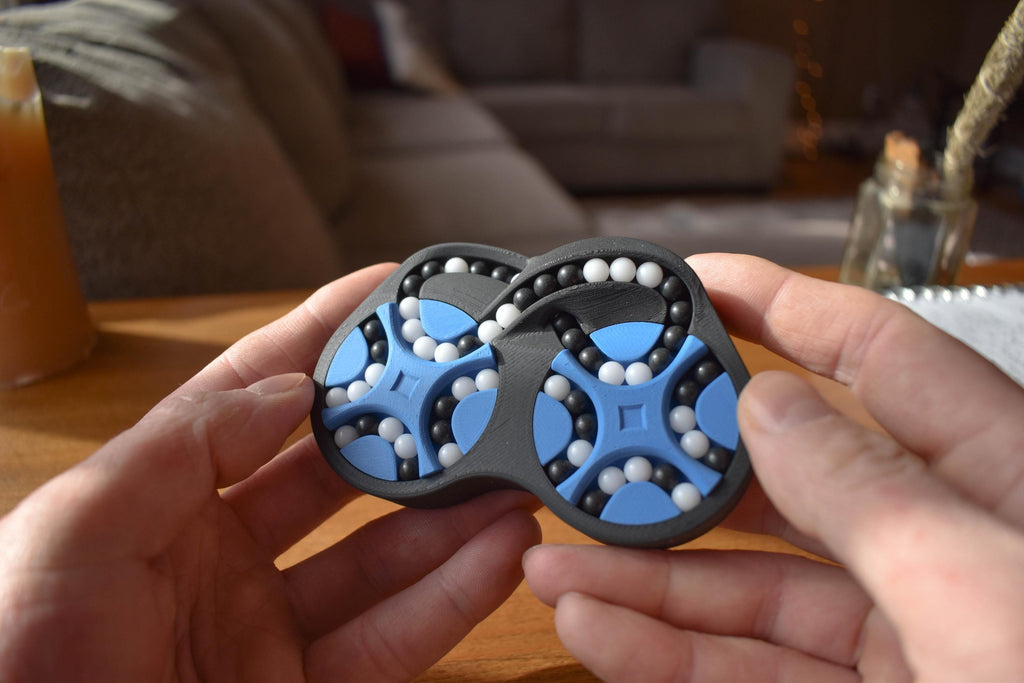 Two-color blue and black mechanical puzzle with rotating gears held in hands, brainteaser fidget toy. - andEleven - The Figure-Eight (2-Color)