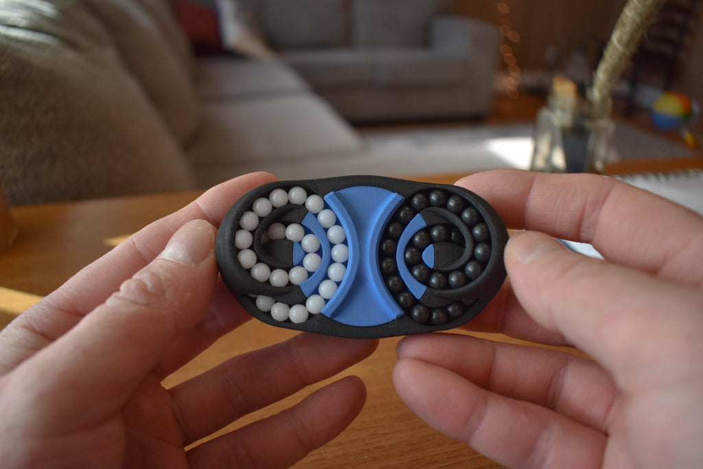Compact black and blue mechanical puzzle brainteaser fidget held in hands on wooden table background. - andEleven - The Butterfly