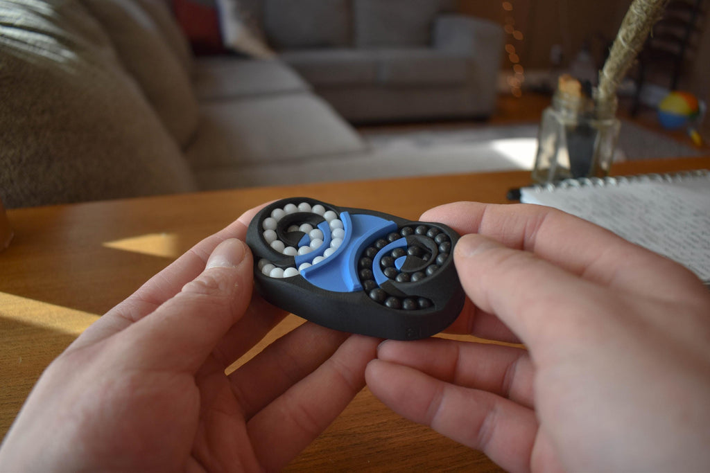 Black and blue butterfly-shaped mechanical puzzle fidget held in hands, brainteaser toy. - andEleven - The Butterfly
