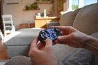Compact blue mechanical puzzle fidget with interconnected butterfly wing pieces held in hands on sofa. - andEleven - The Butterfly