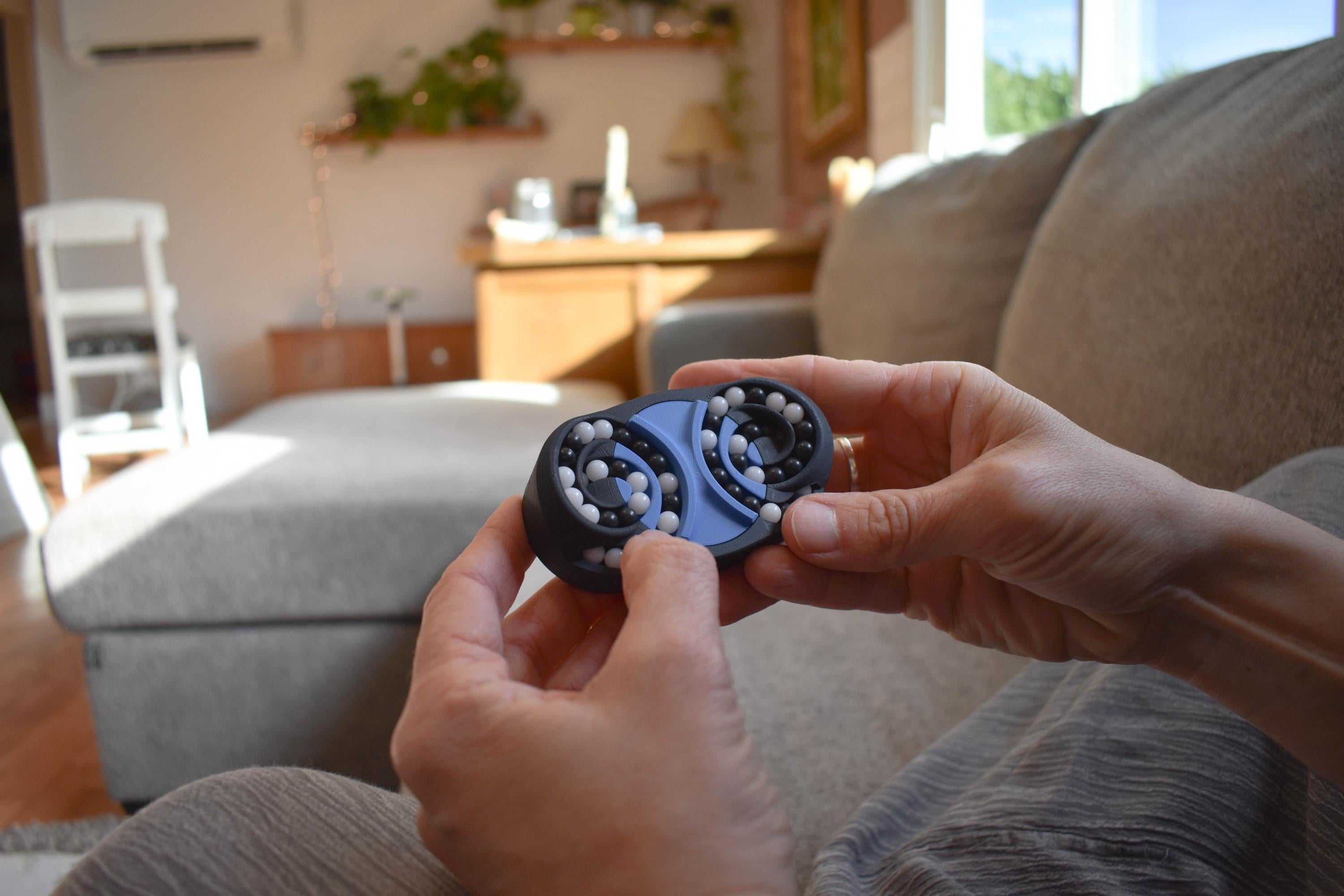 Compact blue mechanical puzzle fidget with interconnected butterfly wing pieces held in hands on sofa. - andEleven - The Butterfly