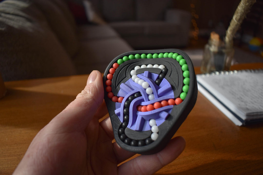 Compact black mechanical puzzle featuring colorful interlocking beads and purple sliding pieces, designed as a brainteaser. - andEleven - The Taurus (4-Color)