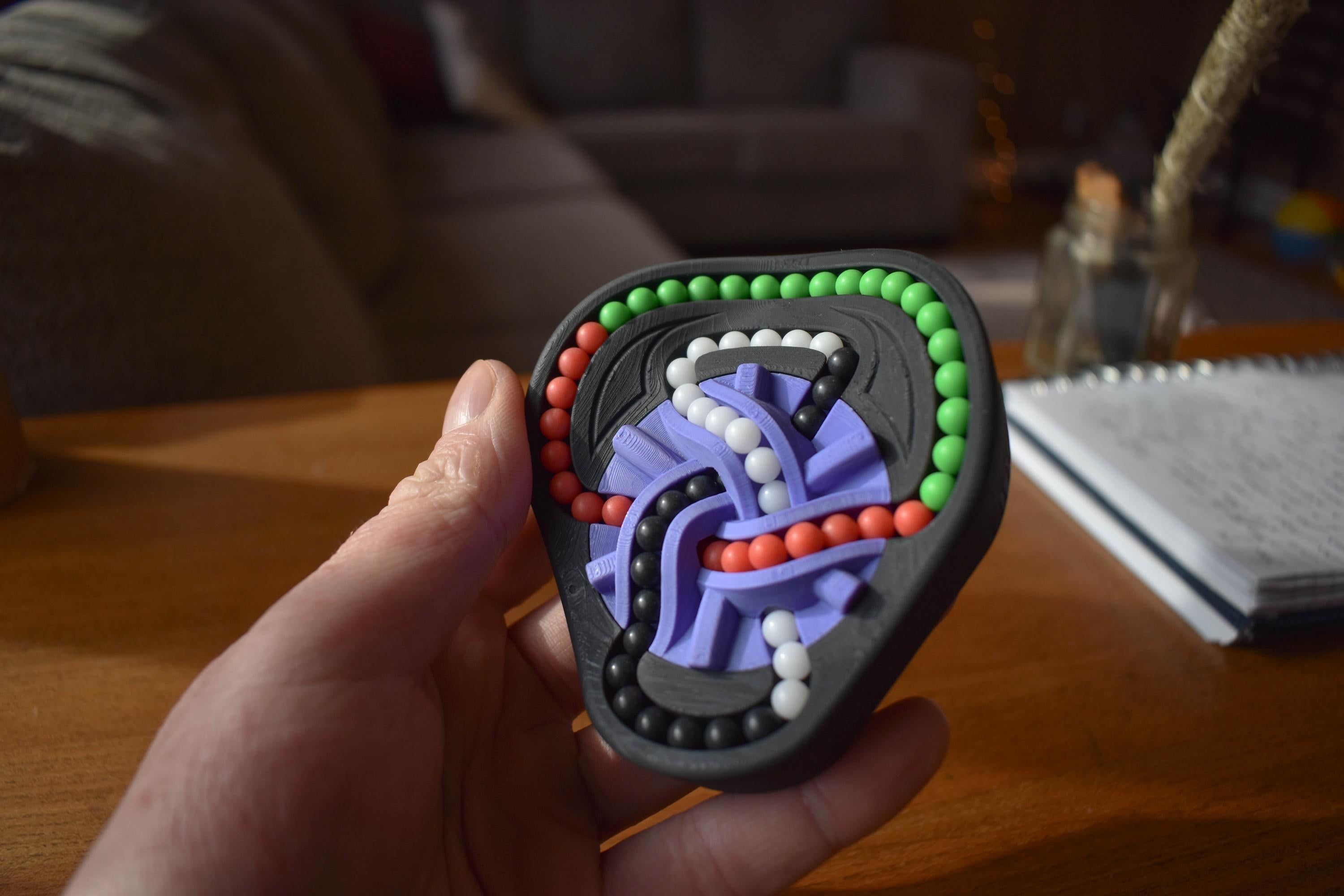 Compact black mechanical puzzle featuring colorful interlocking beads and purple sliding pieces, designed as a brainteaser. - andEleven - The Taurus (4-Color)