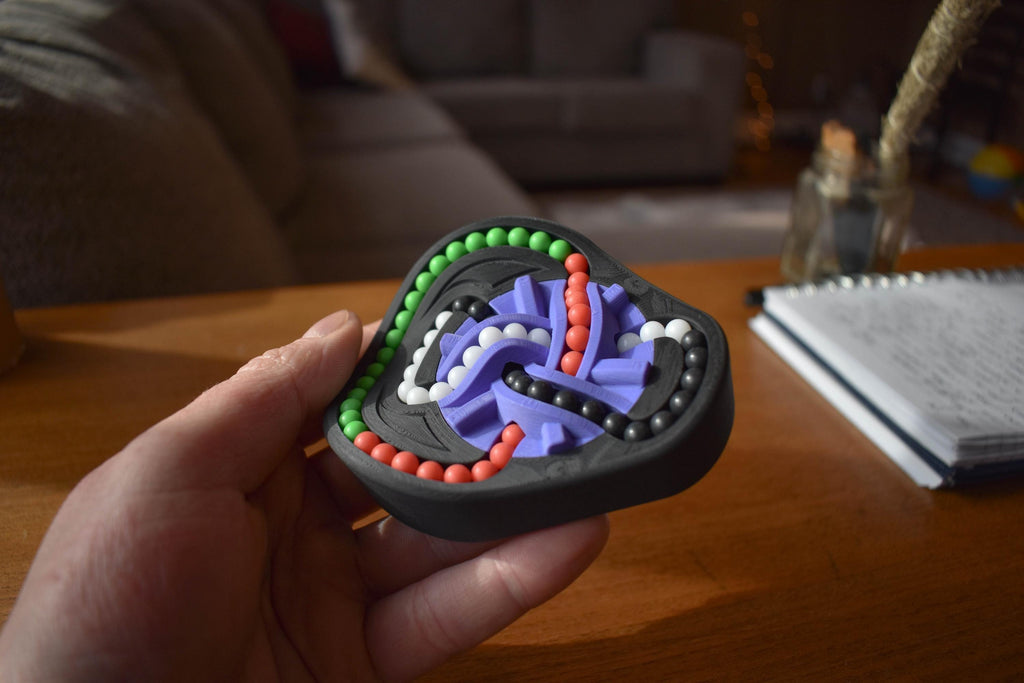 Handheld Taurus mechanical puzzle brainteaser in black with green, red, and purple tracks for fidgeting. - andEleven - The Taurus (4-Color)