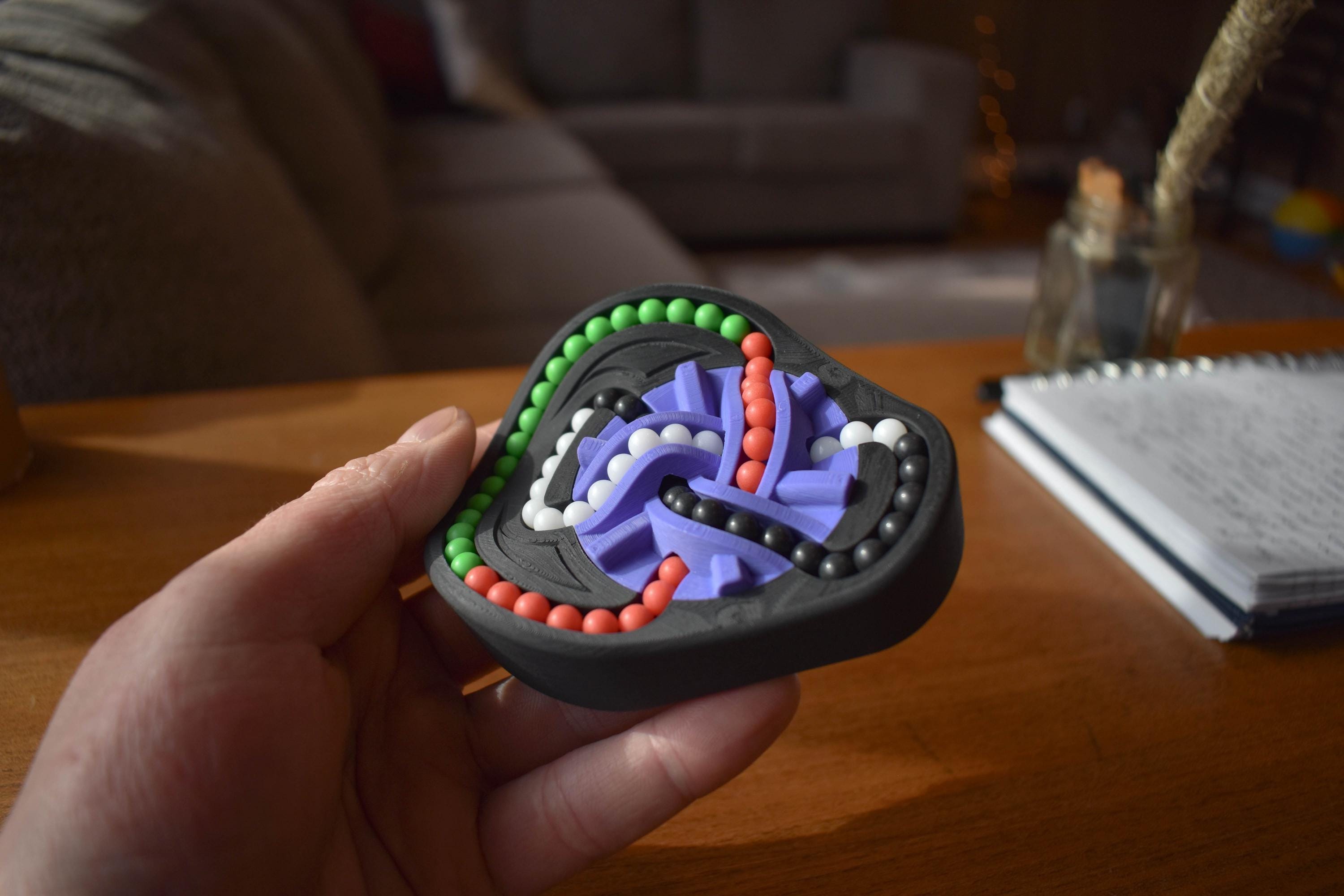 Handheld Taurus mechanical puzzle brainteaser in black with green, red, and purple tracks for fidgeting. - andEleven - The Taurus (4-Color)