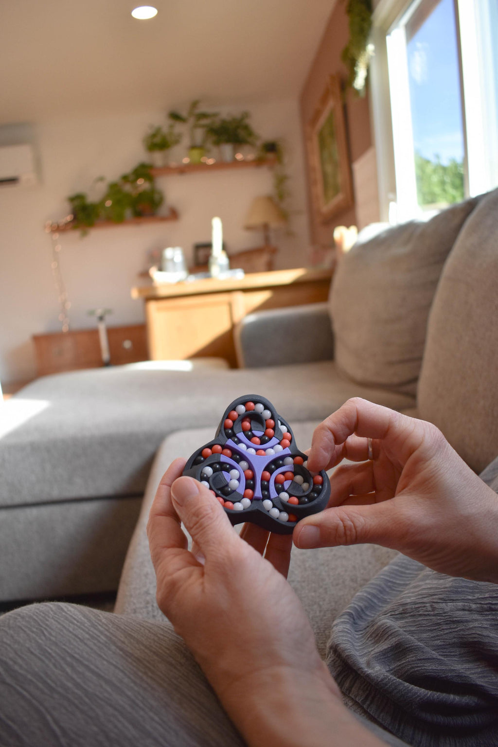 Triad mechanical puzzle brainteaser fidget with black and red rotating gears held in hands on couch background. - andEleven - The Triad