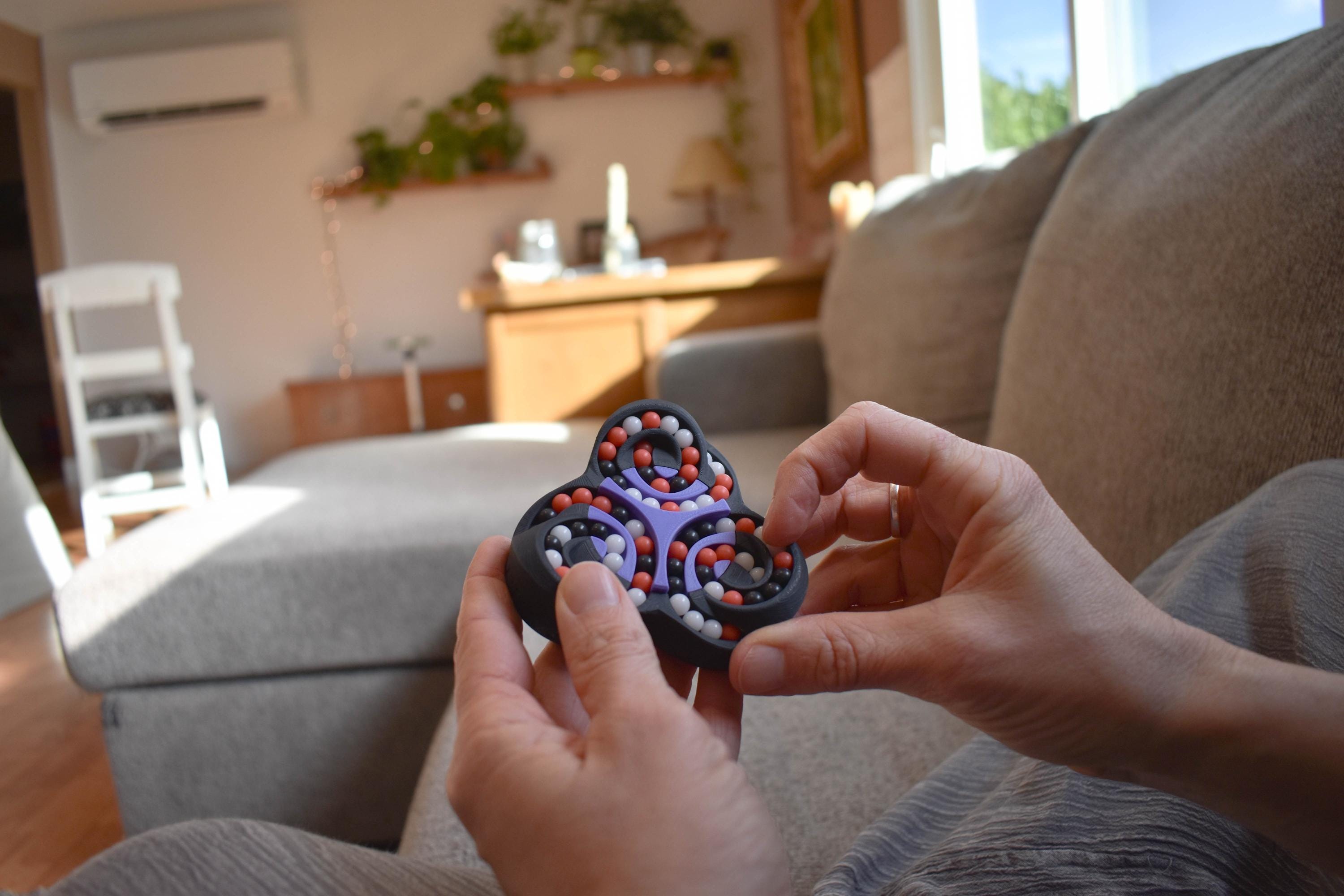 Black and red mechanical puzzle Triad brainteaser fidget held in hands on couch background. - andEleven - The Triad