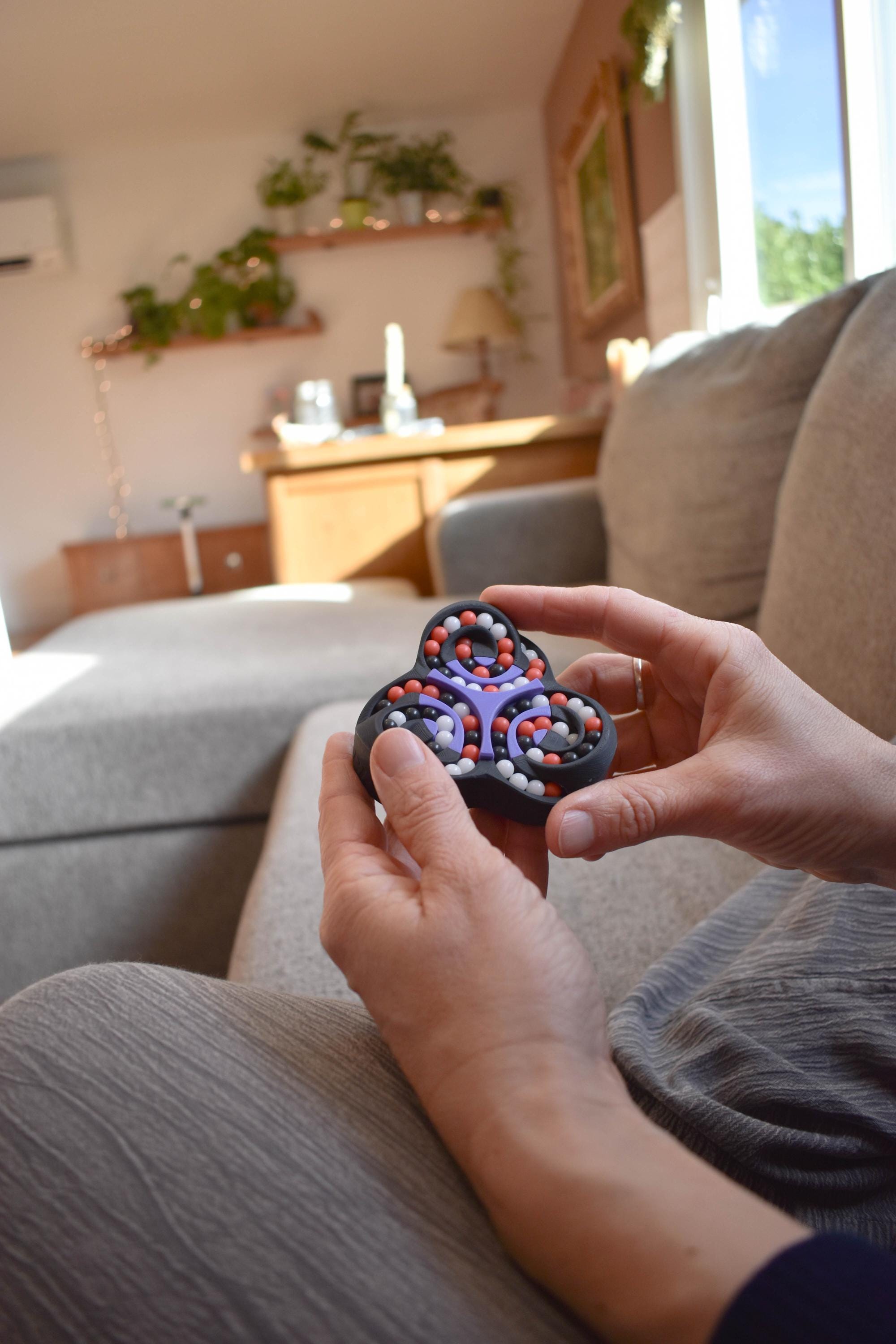 Black and red triangular mechanical puzzle held as a brainteaser and fidget toy in hands. - andEleven - The Triad