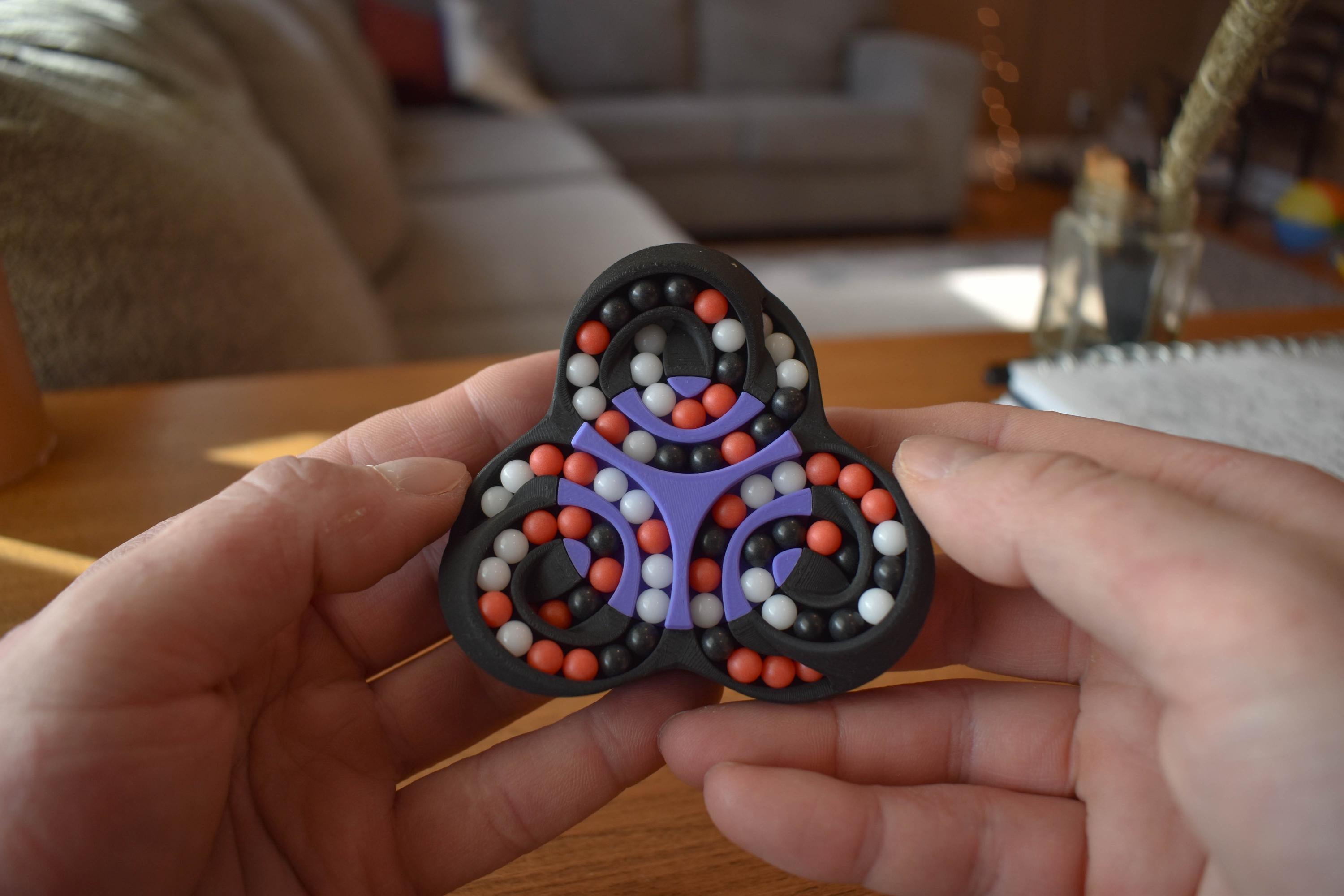 Black triangular fidget with purple tracks and orange and white beads mechanical puzzle brainteaser held in hands. - andEleven - The Triad