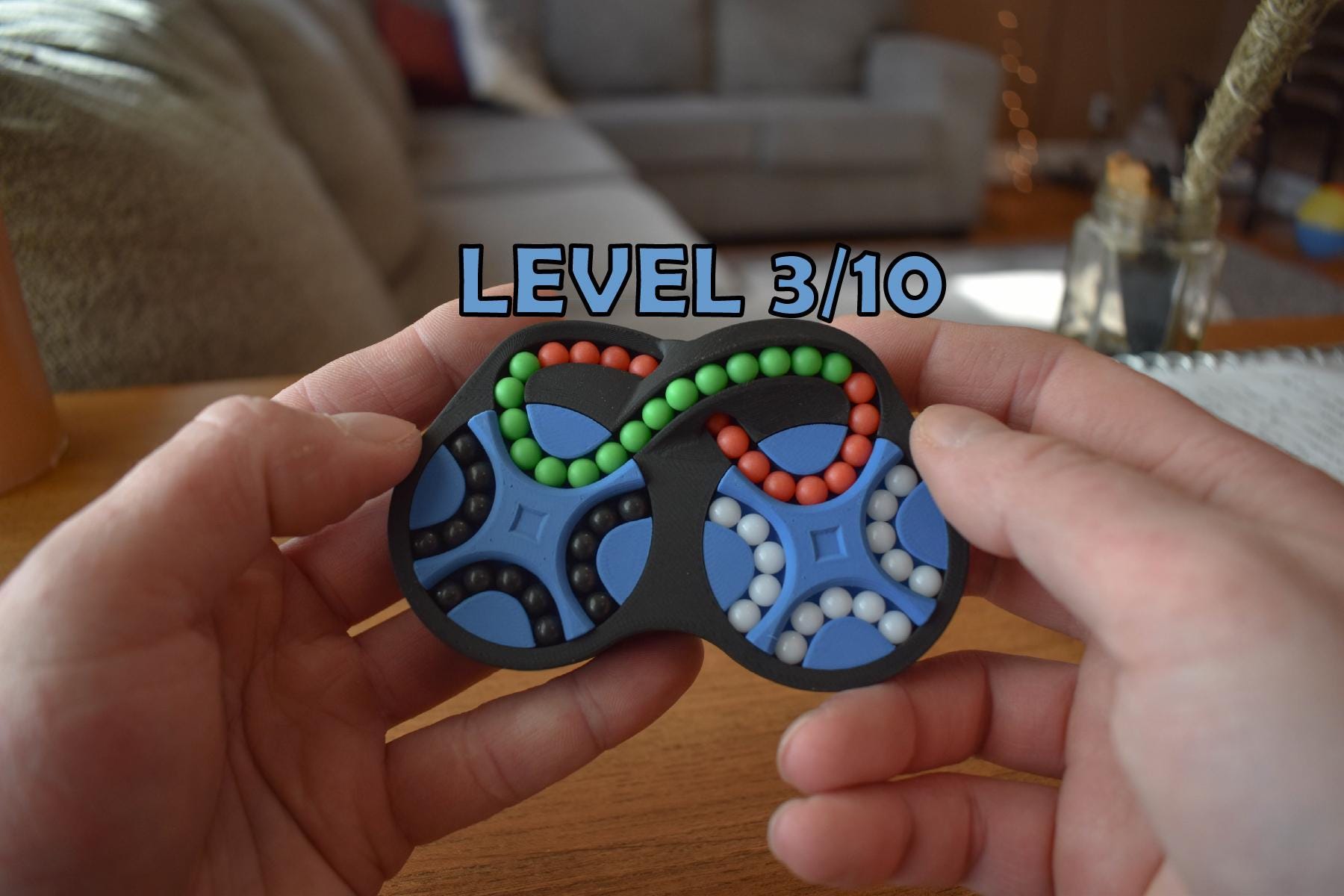 Compact four-color mechanical puzzle with interconnected beads arranged in a figure-eight pattern, a challenging brainteaser . - andEleven - The Figure-Eight (4-Color)