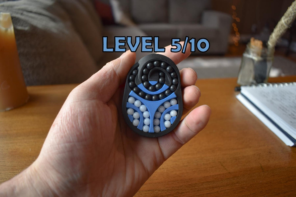 Compact black and blue mechanical puzzle brainteaser held in hand, designed as a fidget toy showing Level 5/10 challenge. - andEleven - The Pretzel