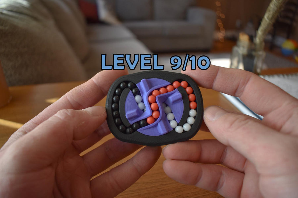 Compact black mechanical puzzle with purple, orange, and pink pieces, held in hands, labeled Level 9/10 brainteaser fidget. - andEleven - The Infinity (3-Color)