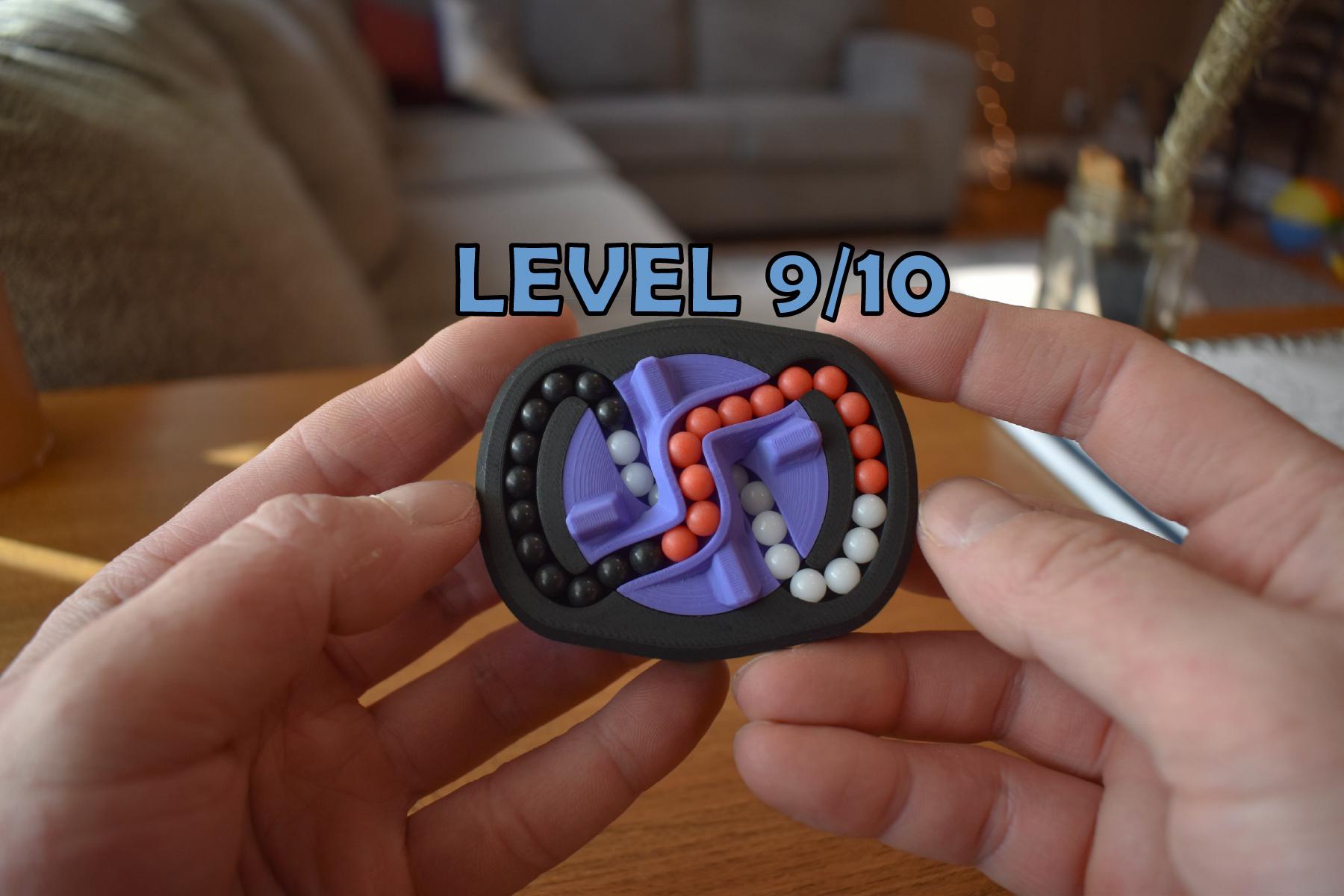 Compact black mechanical puzzle with purple, orange, and pink pieces, held in hands, labeled Level 9/10 brainteaser fidget. - andEleven - The Infinity (3-Color)