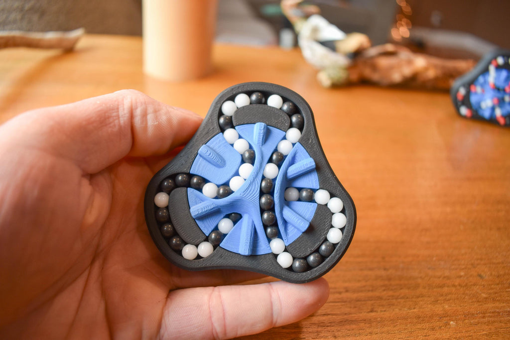 Black and blue mechanical puzzle brainteaser fidget with white beads held in hand. - andEleven - The Delta (2-Color)