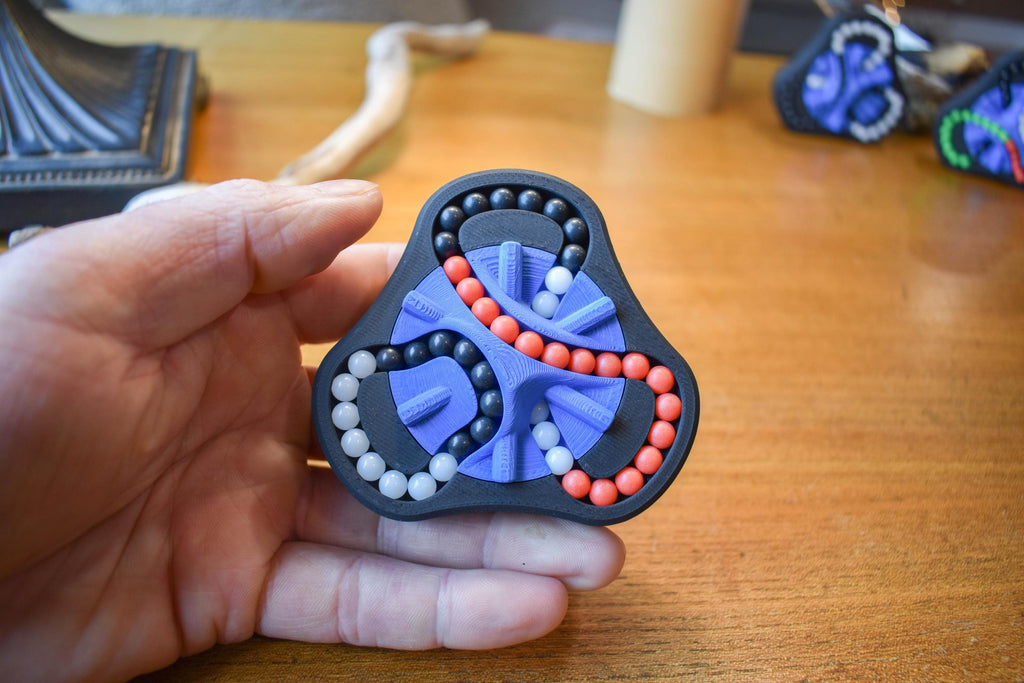 Black triangular mechanical puzzle with red, blue, and gray bead tracks held in hand, brainteaser fidget toy. - andEleven - The Delta (3-Color)
