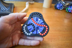 Black triangular mechanical puzzle with red, blue, and gray bead tracks held in hand, brainteaser fidget toy. - andEleven - The Delta (3-Color)