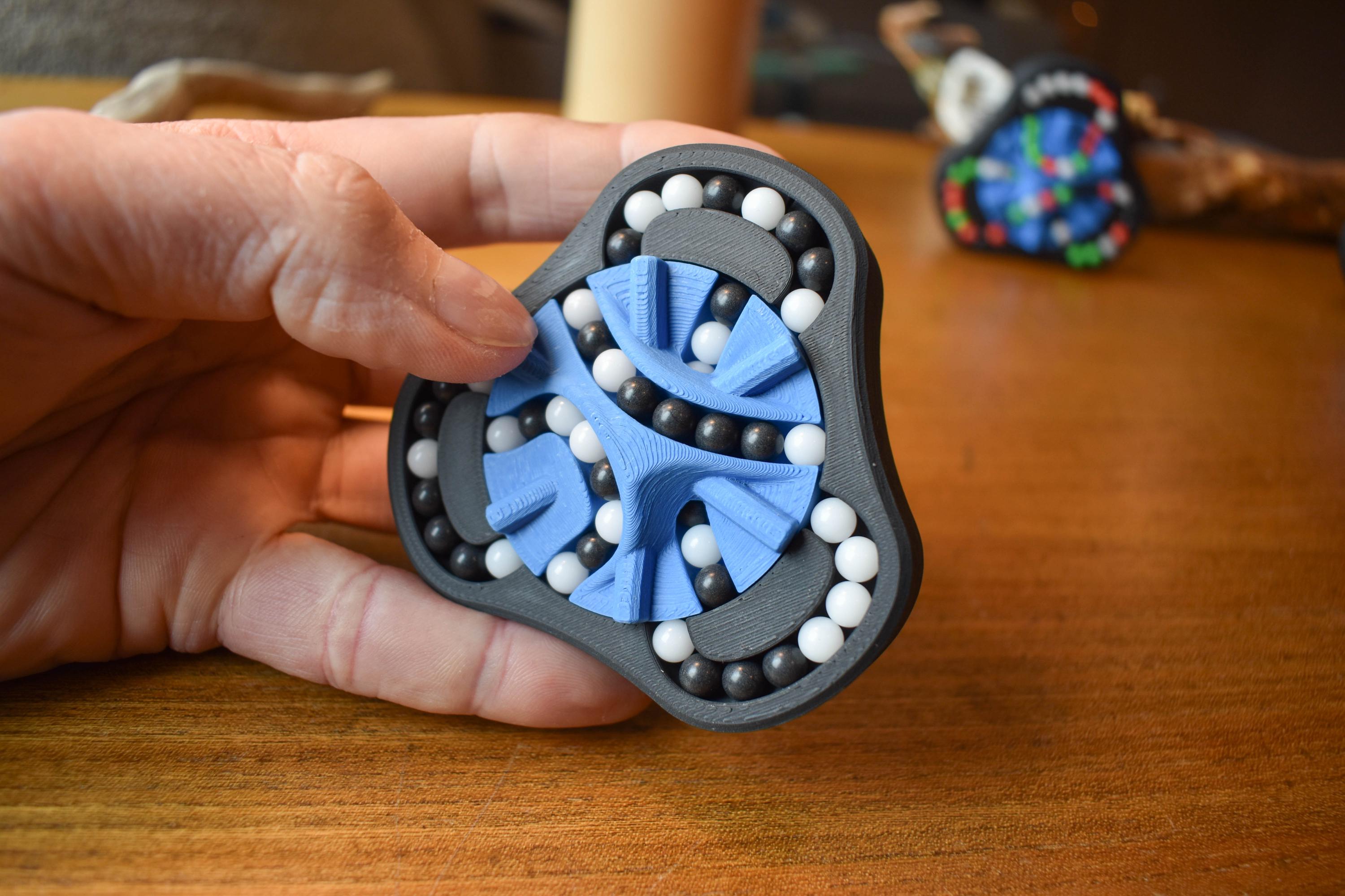 Handheld black and blue mechanical puzzle brainteaser with white beads for fidgeting. - andEleven - The Delta (2-Color)