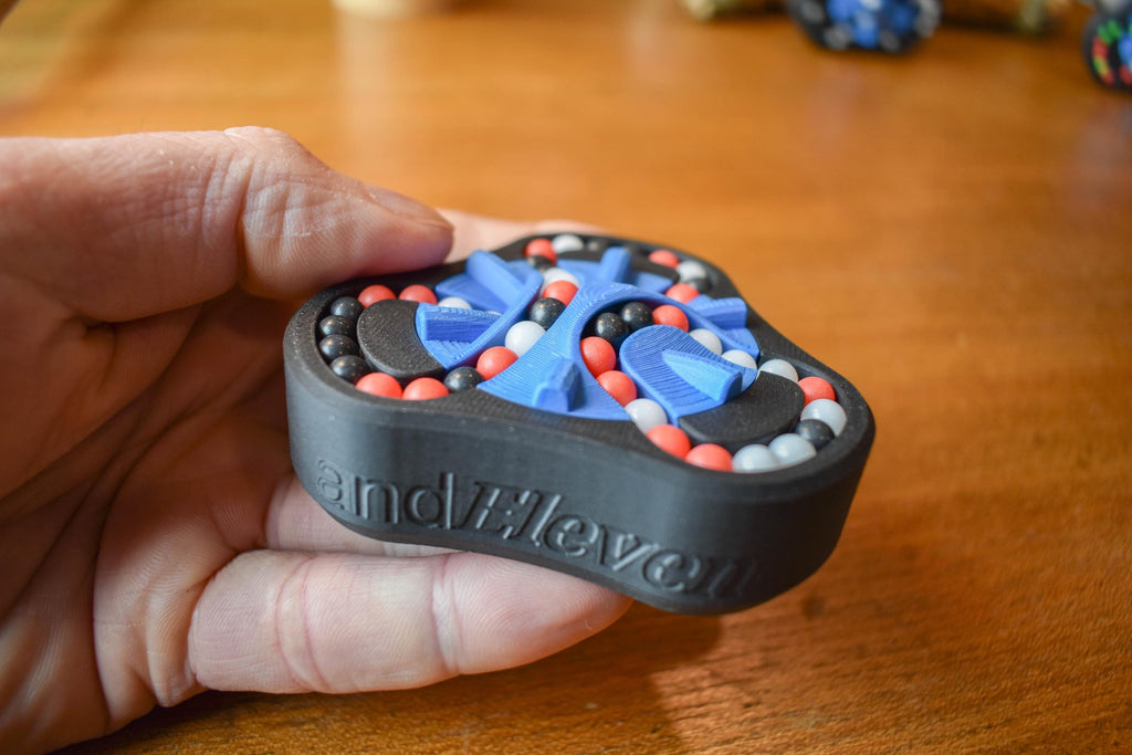 Black mechanical puzzle with blue and orange beads, labeled The Delta, handheld brainteaser fidget toy. - andEleven - The Delta (3-Color)