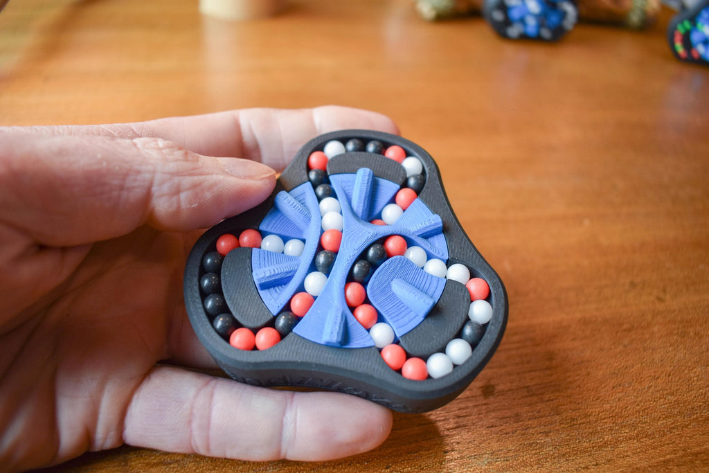 Hand holding a black triangular mechanical puzzle with blue, red, and white beads for brainteaser and fidget use. - andEleven - The Delta (3-Color)